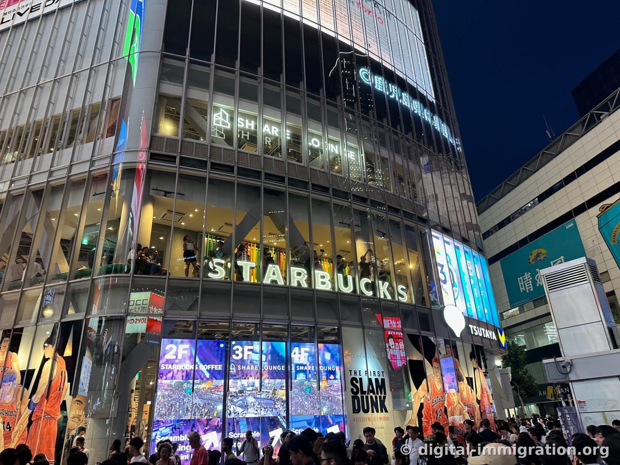 夜に明かりを灯したQFRONT建物、2階のSTARBUCKS看板と3・4階のSHARE LOUNGE、1階のTSUTAYA看板