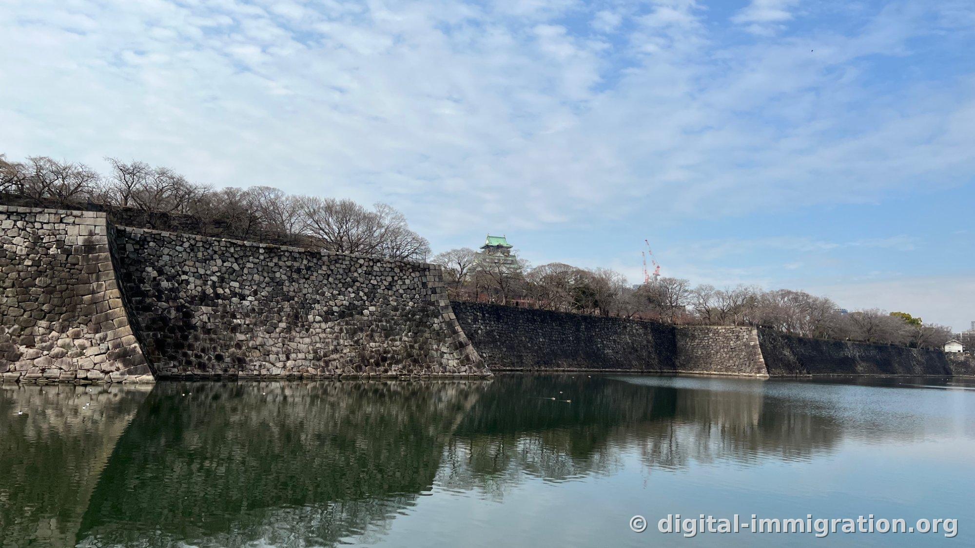 Le fossé du château d'Osaka et le mur de pierre noire empilé en biais, le toit vert patine de la tour de guet entrevuapparaissant légèrement entre les arbres contre un ciel bleu