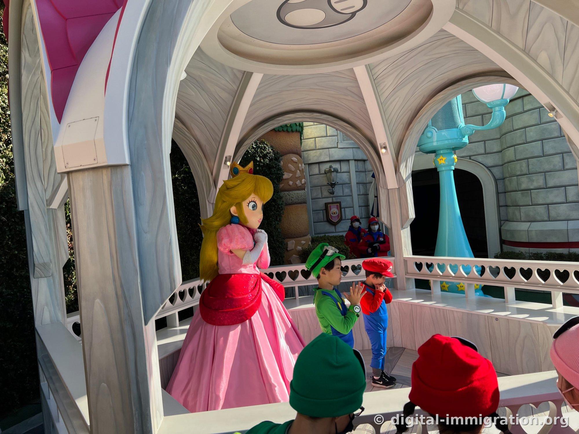 Princess Peach in a pink dress faces two children wearing Luigi and Mario hats inside a white gazebo with heart-patterned railings