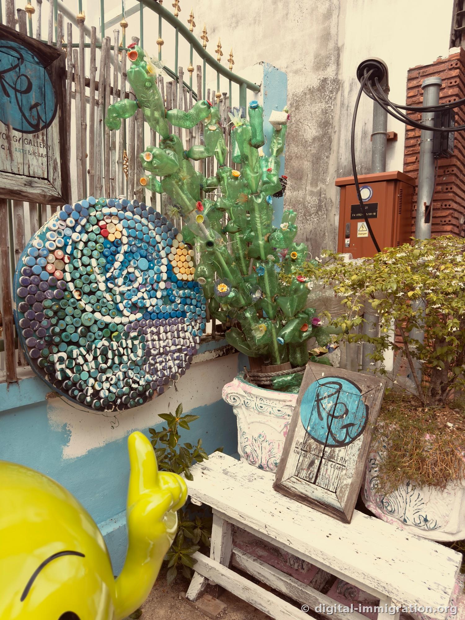 Circular mosaic artwork made from bottle caps and green cactus sculpture made from cut plastic bottles, RAYONG GALLERY wooden sign