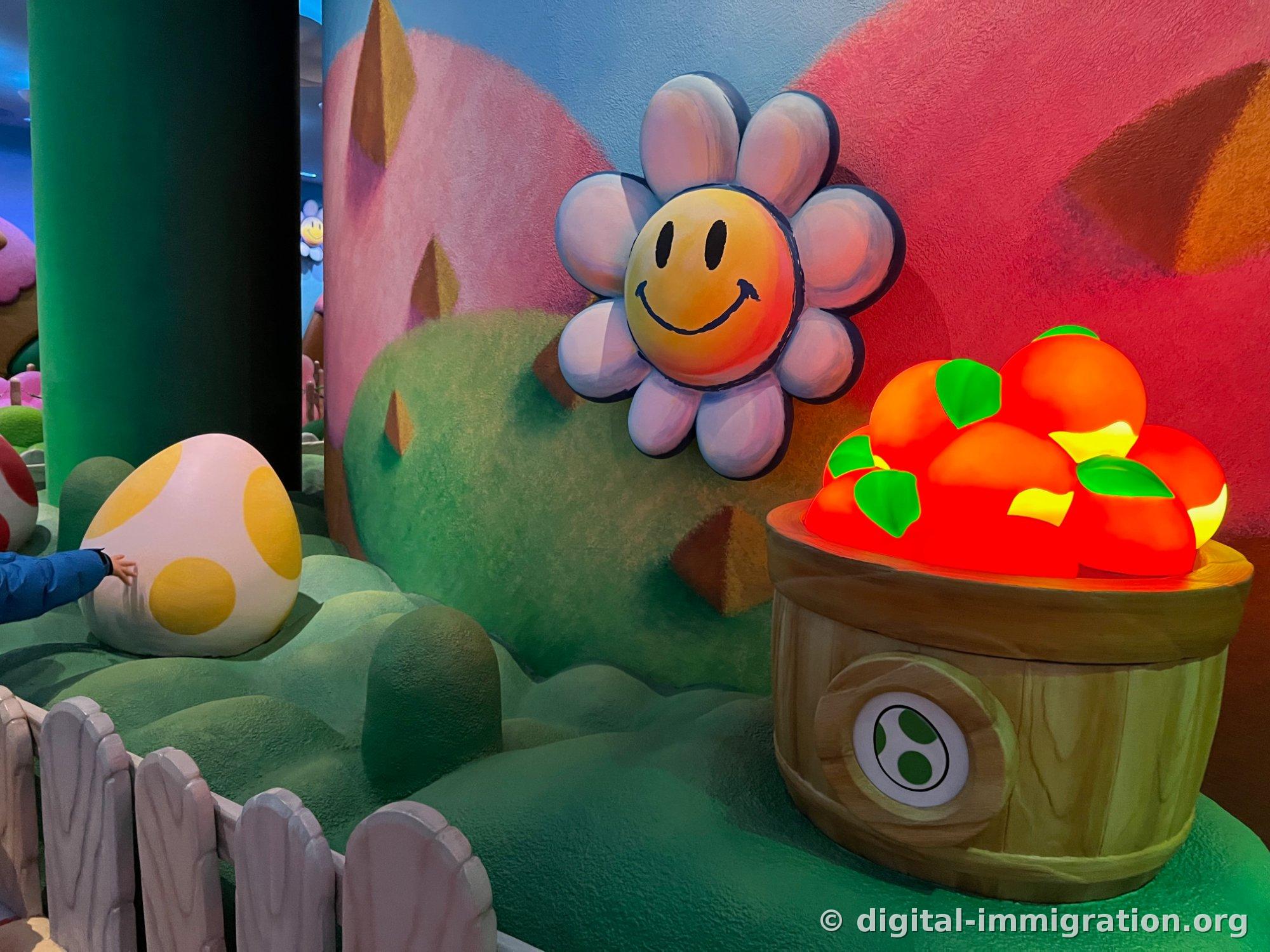 Yellow spotted Yoshi egg and smiling white flower wall decoration, with a wooden barrel sculpture full of red apples topped with green leaves
