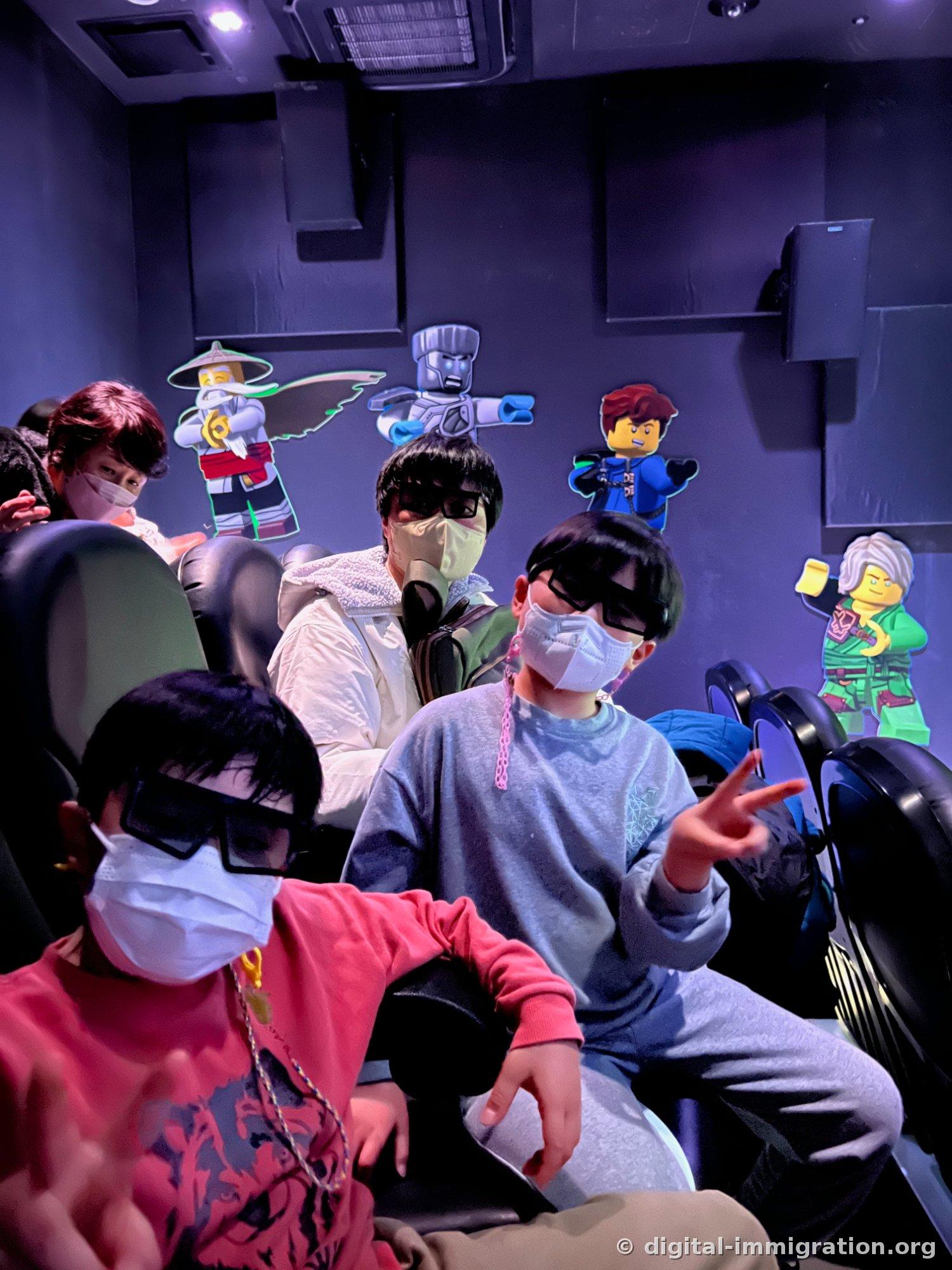 4D上映館の座席で黒い3D眼鏡をかけた子どもたちが座っており、壁面にニンジャゴーキャラクターの絵が貼ってある