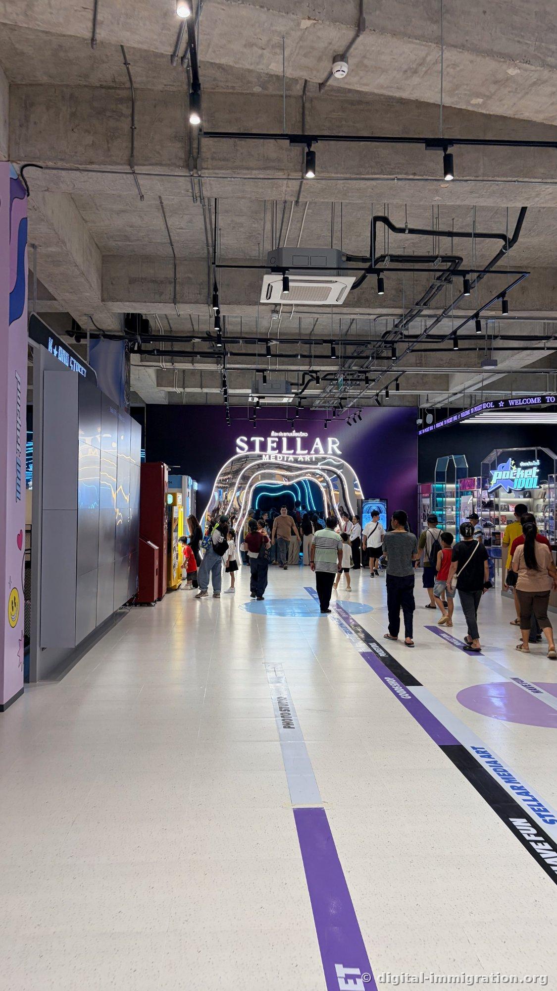 STELLAR MEDIA ART neon tunnel entrance and POCKET IDOL merchandise store on right, colored zone guide lines on floor