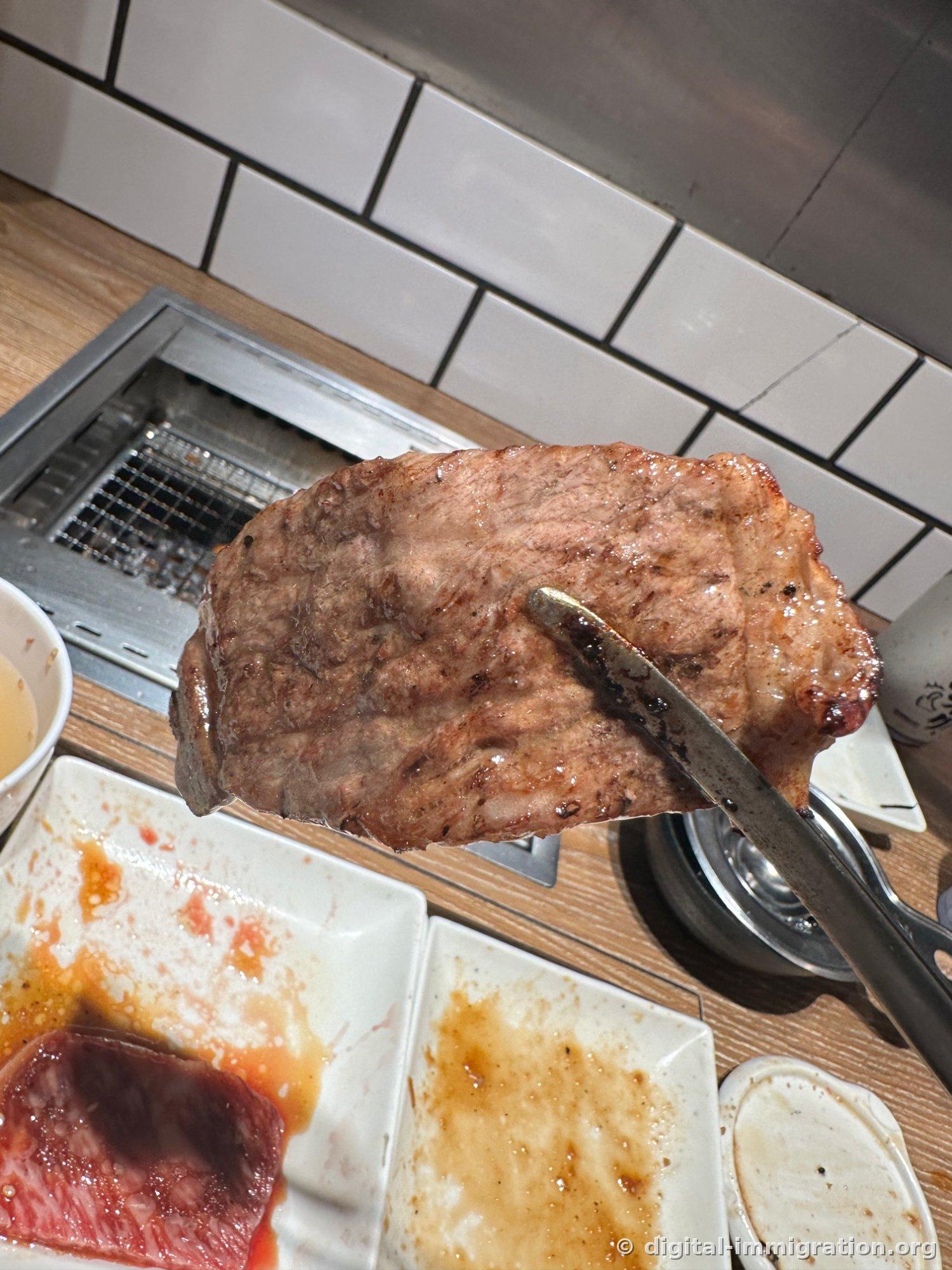 Un gros morceau de wagyu cuit à point tenu à la pince, avec les marques de la grille sur la surface, et l'assiette suivante de viande en dessous