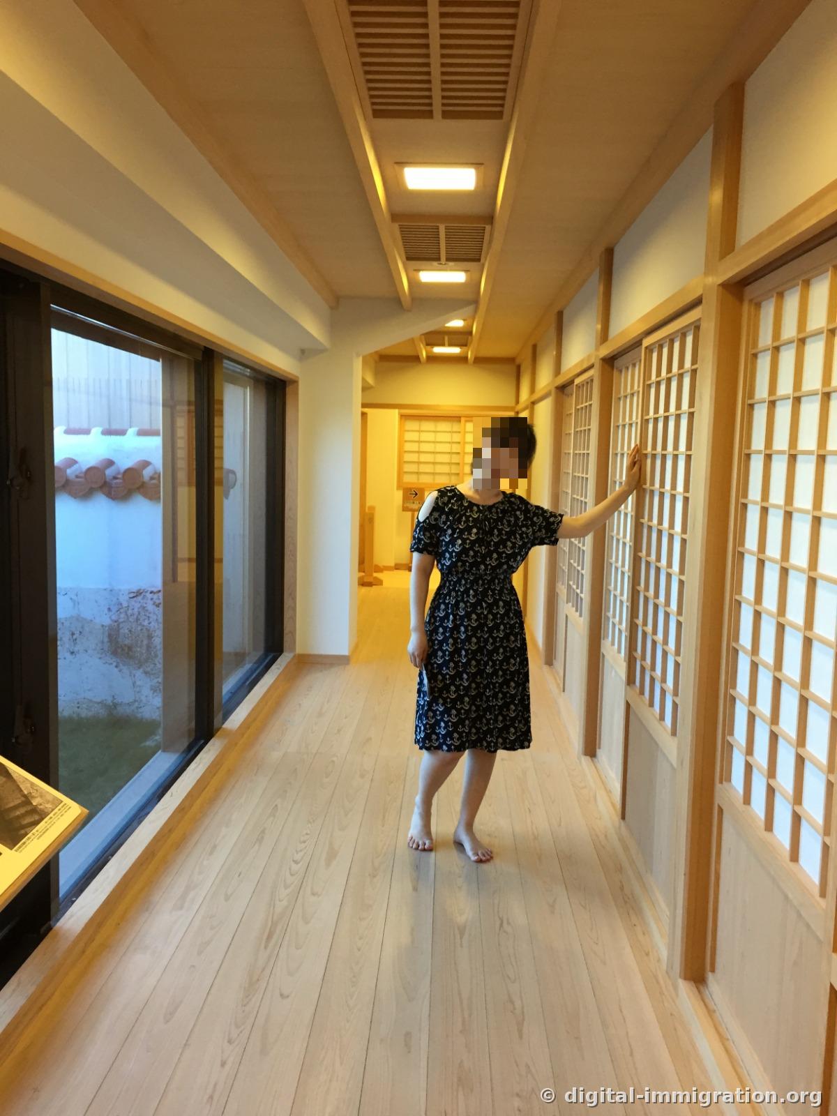 A person walking barefoot through a restored building corridor with bright wooden flooring and lattice windows