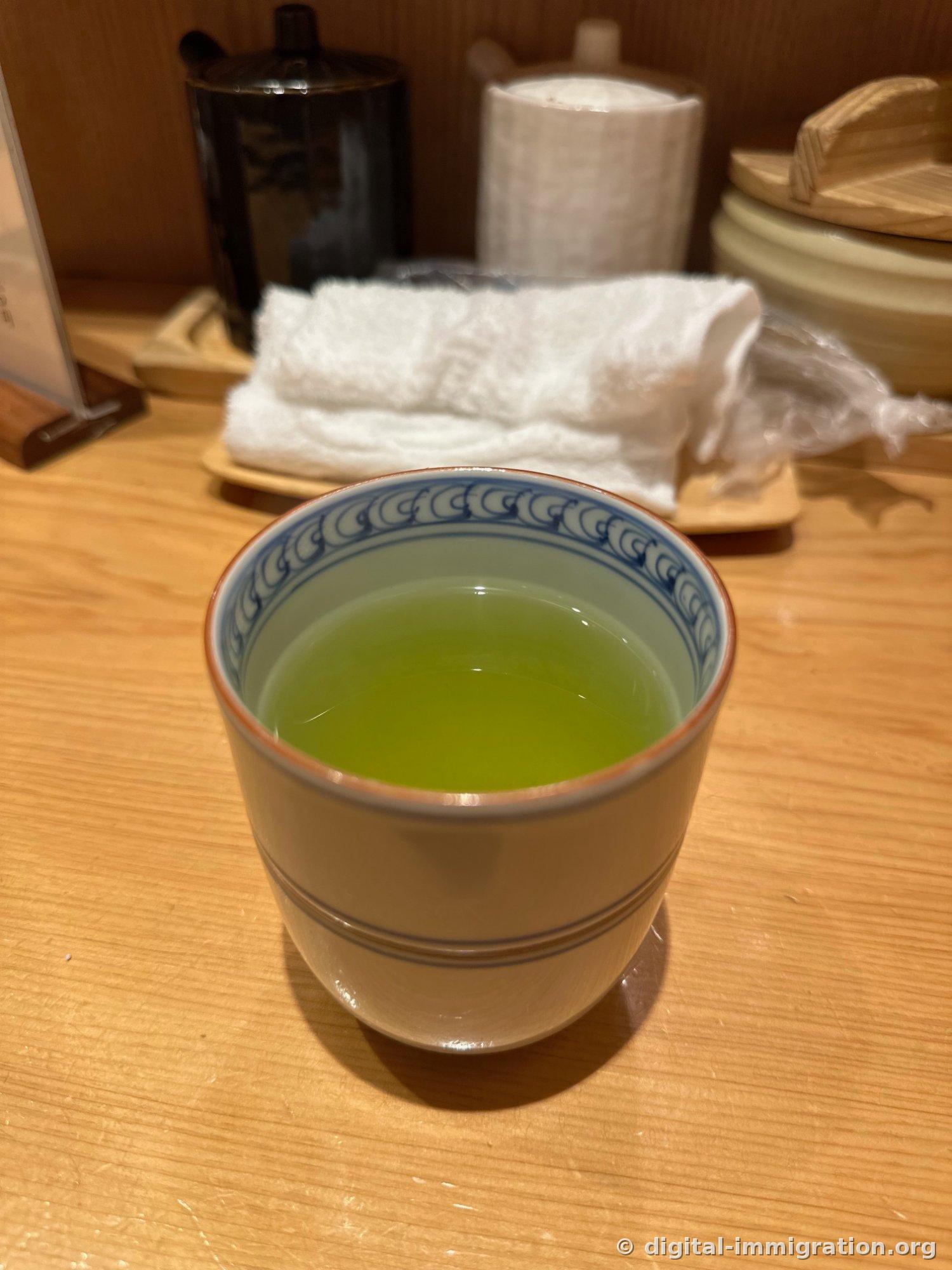 放在桧木吧台上厚陶瓷杯里的浅绿色绿茶，后面是热毛巾和木质饭筒