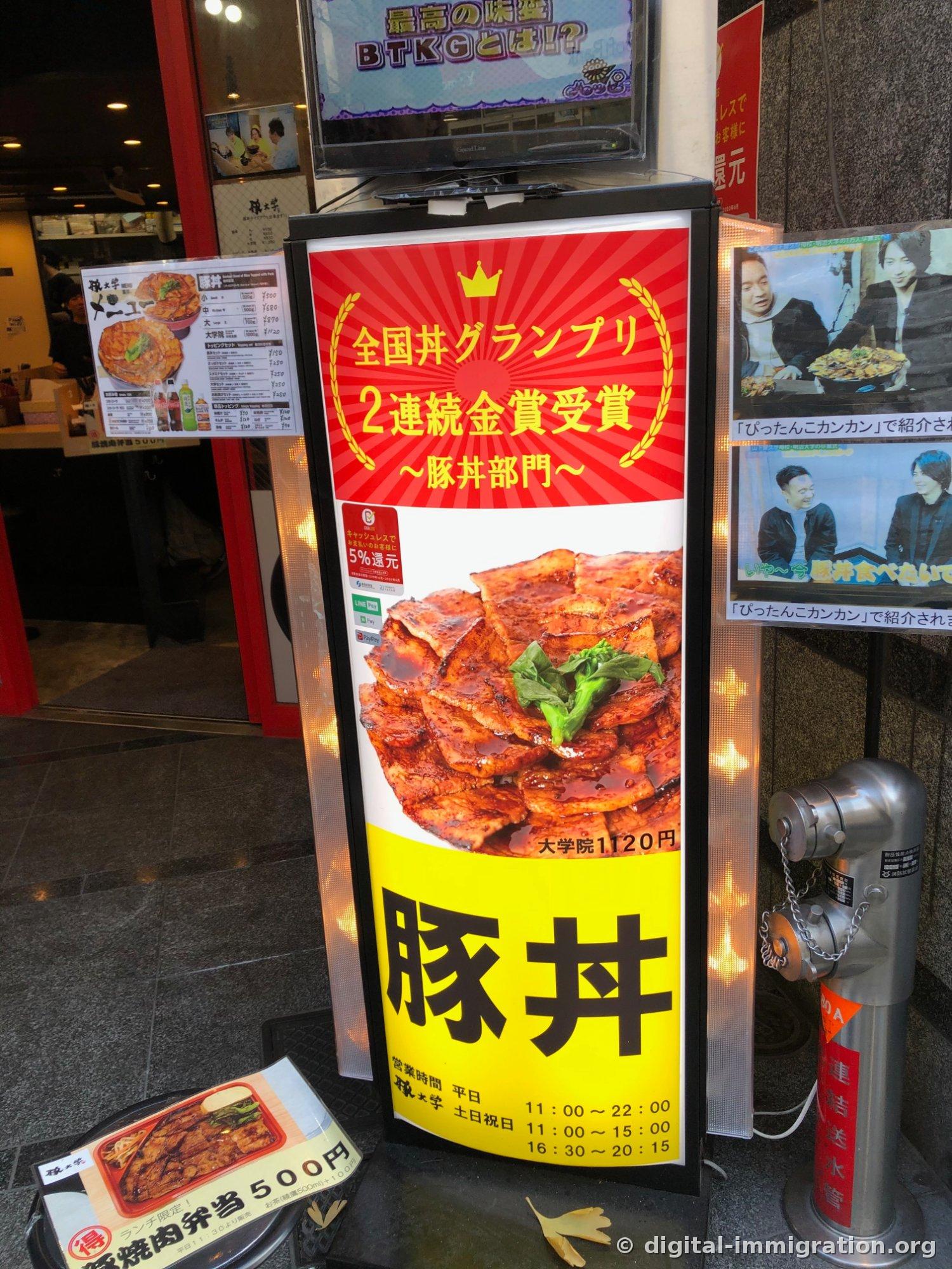 L'enseigne lumineuse devant le restaurant. Elle affiche « 全国丼グランプリ 2連続金賞受賞 豚丼部門 », une photo de bol de porc copieusement garni, « 大学院 1120円 », et les horaires d'ouverture en semaine et week-end