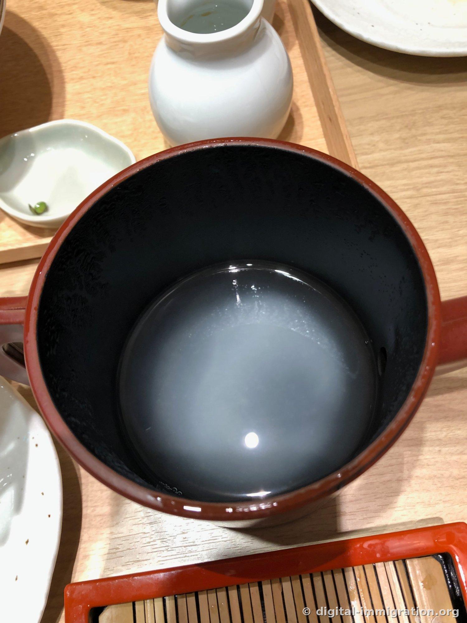Looking down into a crimson lacquered pitcher filled with cloudy grayish-white sobayu