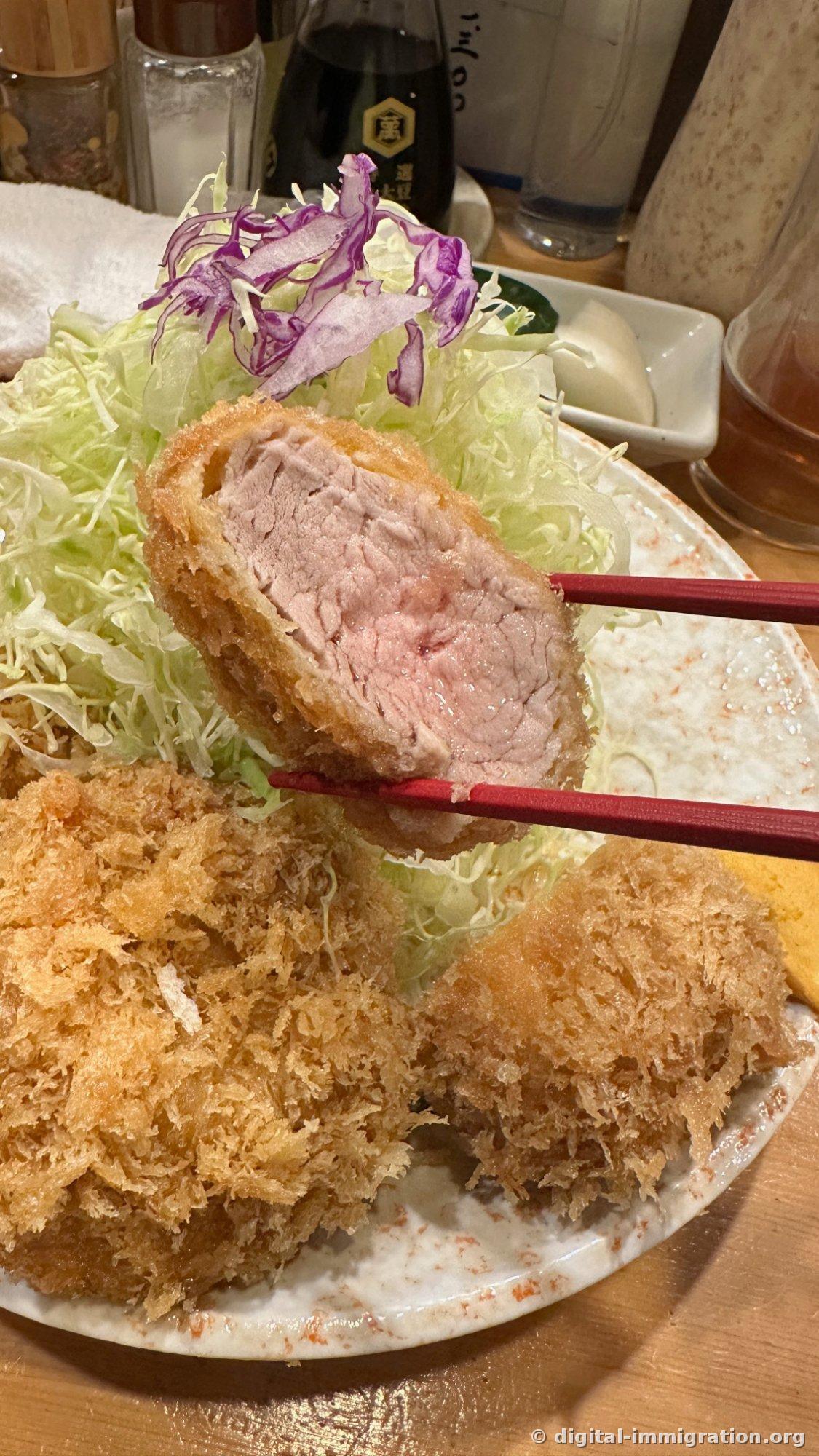 Cross-section of filet cutlet lifted with red chopsticks, showing a light pink center with visible juices