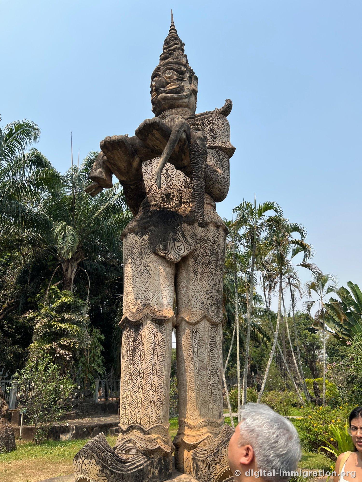 Une vue de bas en haut d'une énorme statue de divinité protectrice avec des motifs en losange densément gravés sur le pantalon