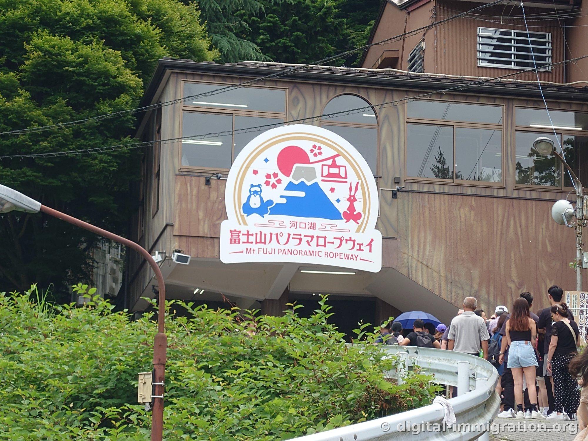 A circular ropeway sign showing a blue tanuki and red rabbit, Mount Fuji, and a gondola, photographed from below