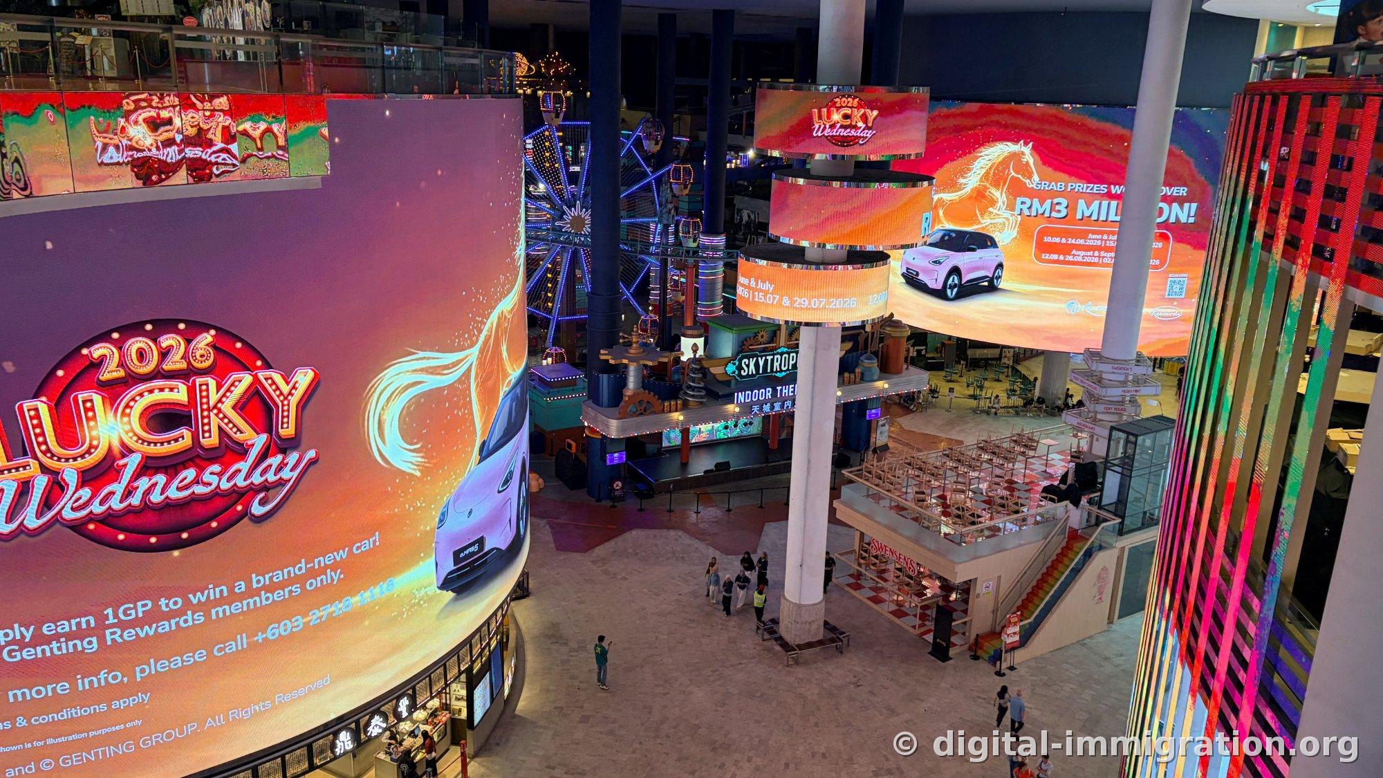 Large curved LED in indoor plaza showing 2026 Lucky Wednesday car prize advertisement with blue-lit Ferris wheel and SKYTROPOLIS sign behind