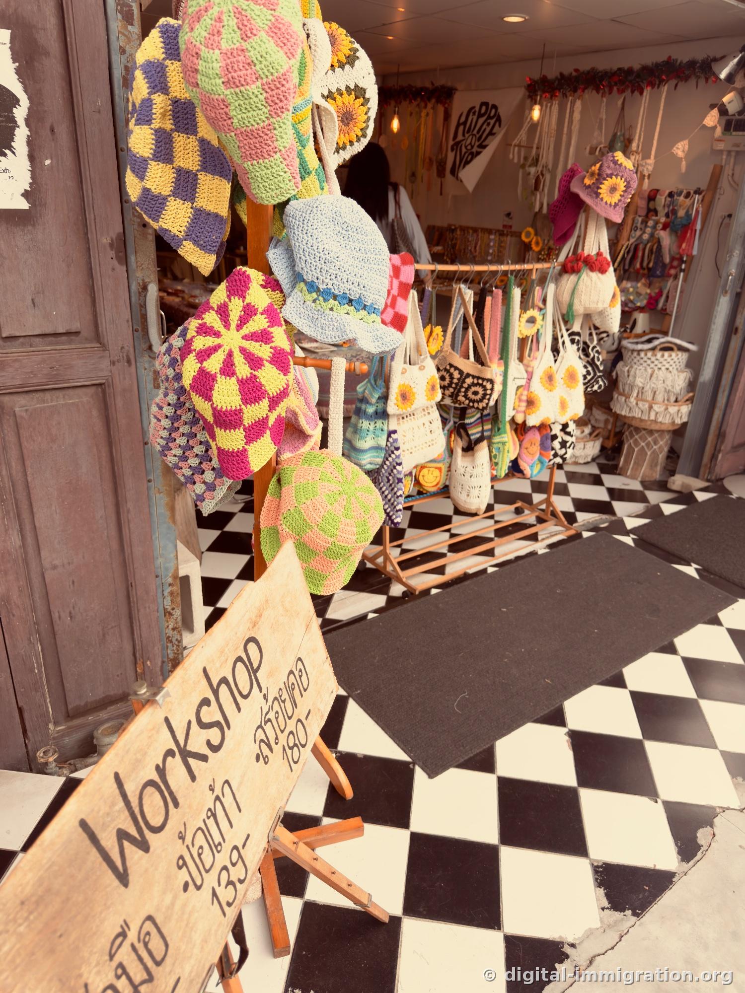 Colorful hand-knitted hats hanging in shop entrance with checkered floor and wooden workshop sign in front