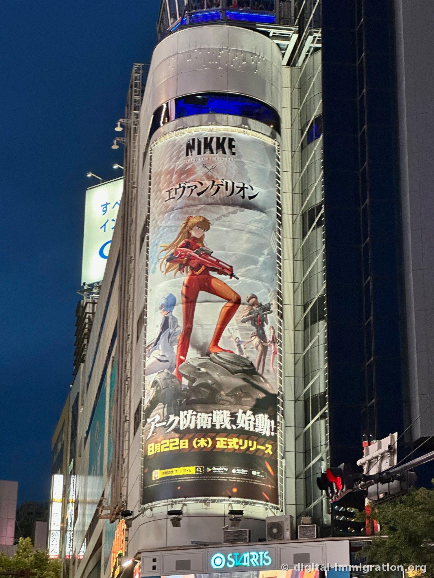 円筒形の建物の外壁を巻いたNIKKEとエヴァンゲリオンのコラボ大型広告、下にSTARTS看板が見える