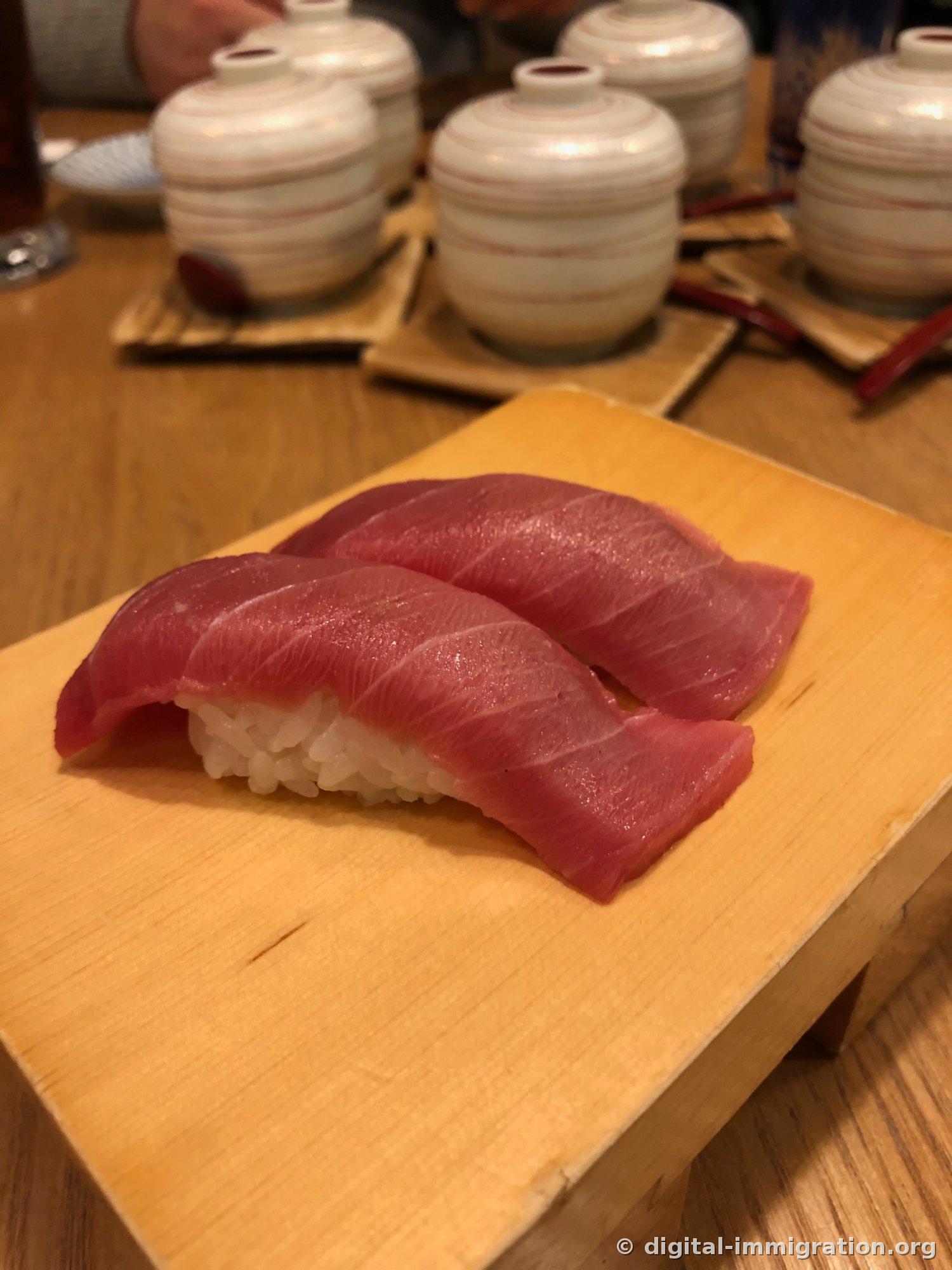 Deux pièces de nigiri de thon avec plusieurs petits bols d'omelette à la vapeur du même motif alignés derrière sur la table