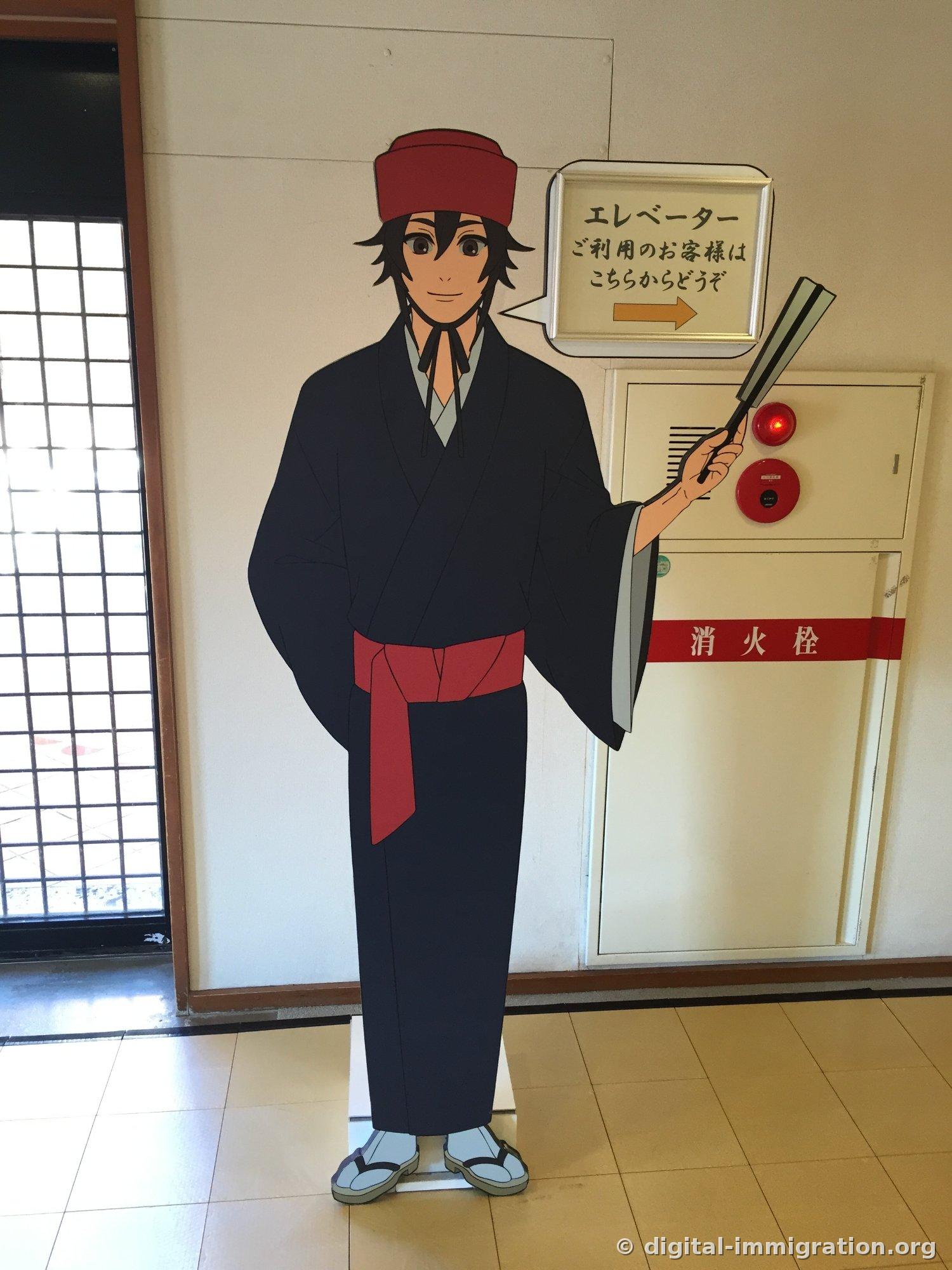 A tall informational sign with a character in Ryukyu dress pointing with a fan, elevator guidance in a speech bubble, fire extinguisher beside it