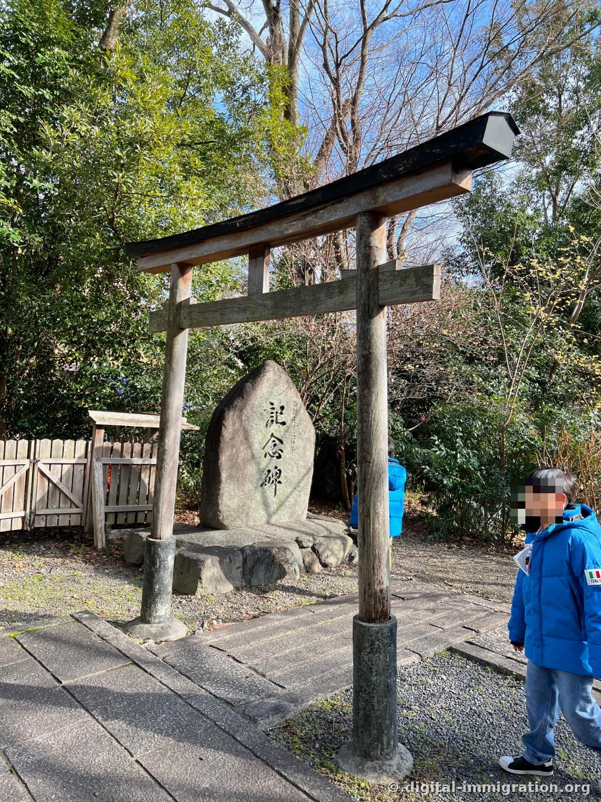 A section of the grounds with a faded wooden torii gate under which a stone monument with '記念碑' carved in large characters sits