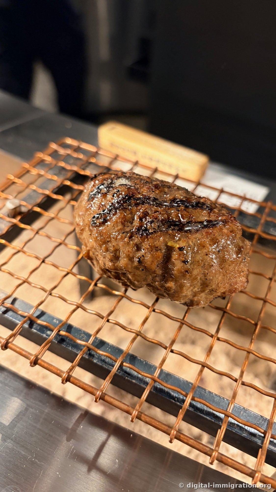 Gros plan d'un hamburger avec les marques de charbon évidentes, posé sur le plateau en treillis de cuivre