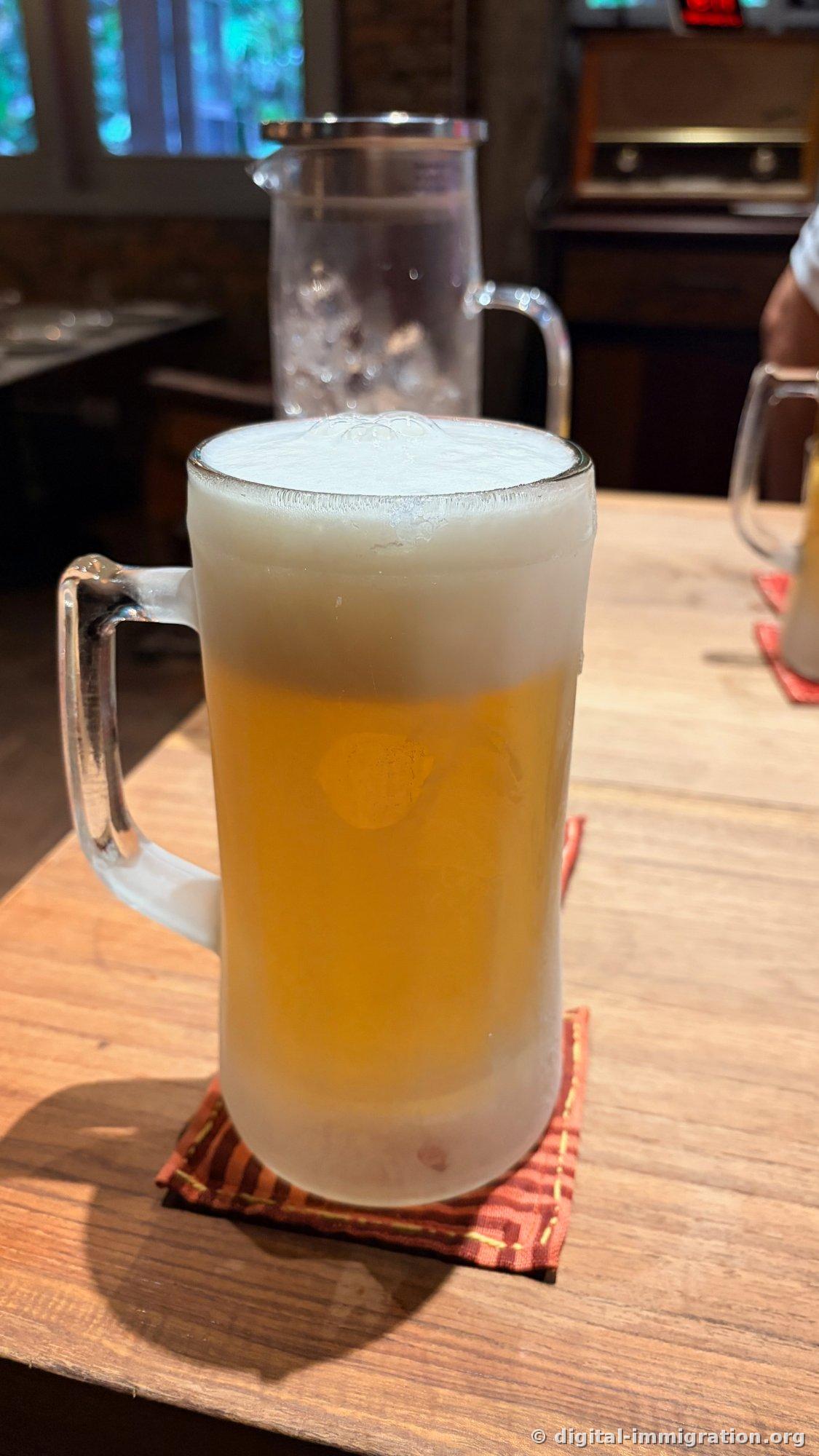 Le verre à bière givré avec bière pression et mousse épaisse, un couvre-verre rouge sur la table en bois et le pichet d'eau glacée dans une prise alternative de la même scène