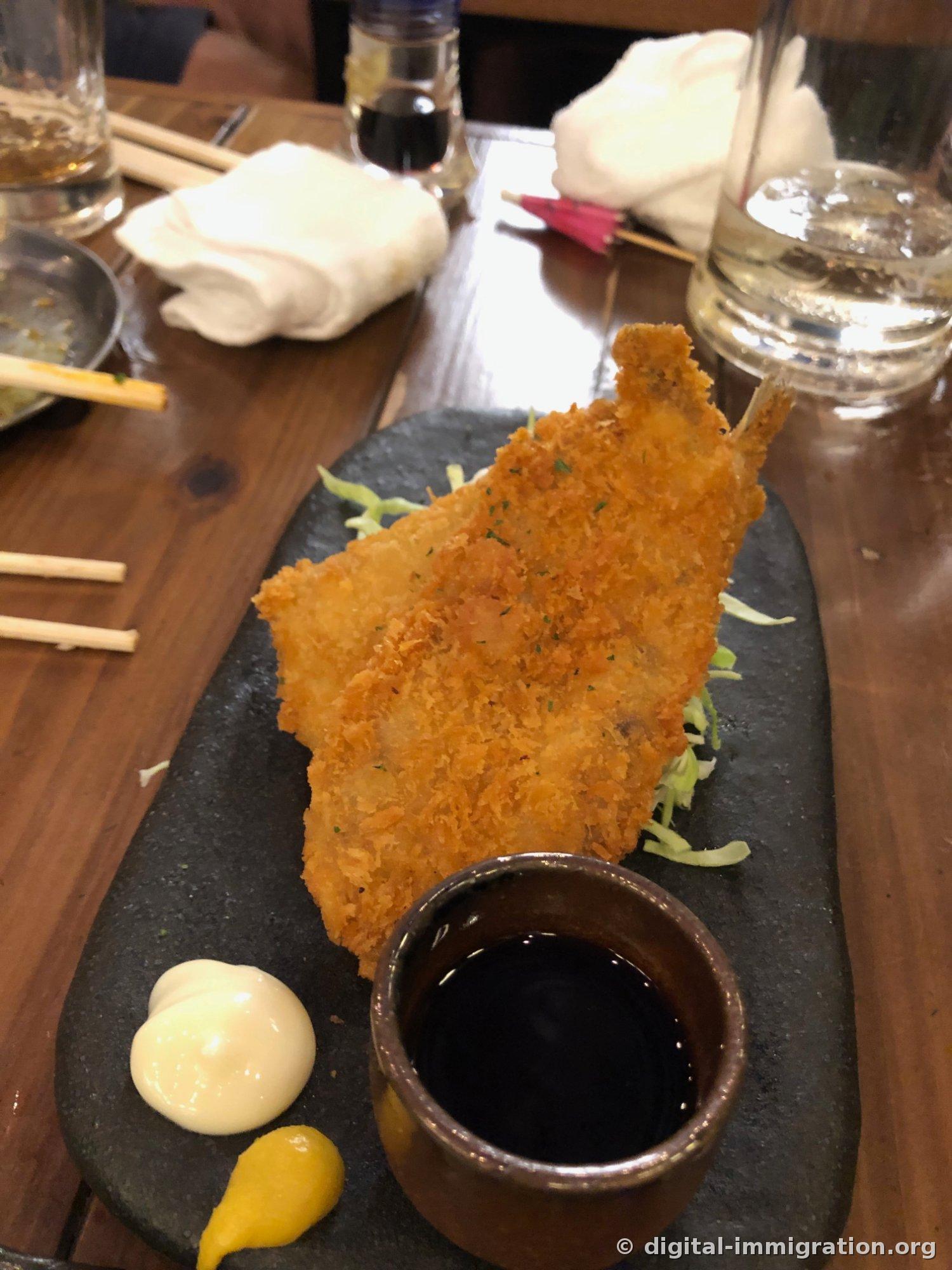 黑色石盘上放着一整条展开炸过的大鱼。面包糠炸得厚厚的，配着切成丝的卷心菜、蛋黄酱、芥末、酱油小碟