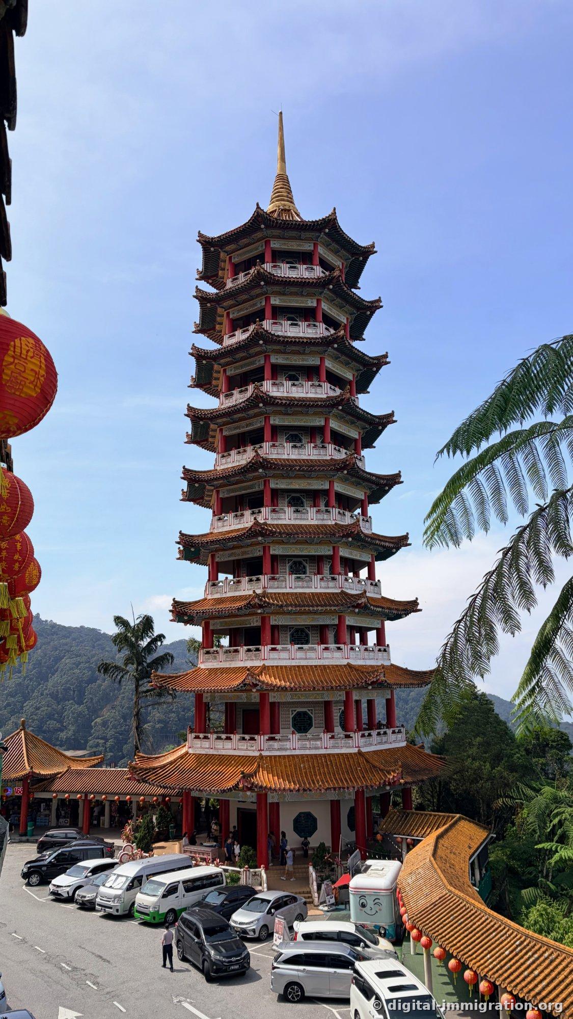 Vue de face de la pagode de 9 étages aux colonnes rouges et tuiles orange, avec des minibus et des voitures alignés dans le parking devant, et des lanternes rouges accrochées à gauche