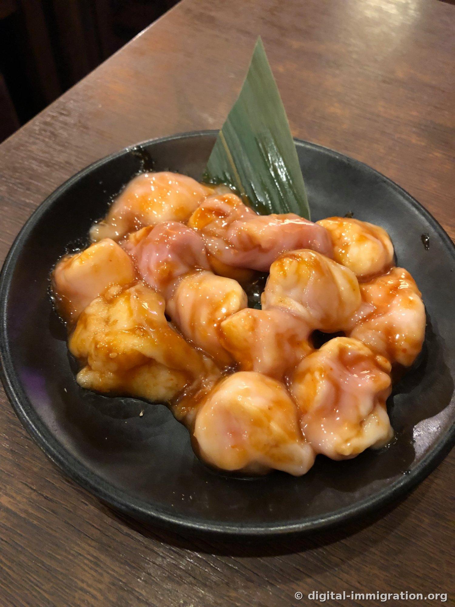 Raw intestine on a black plate with a bamboo leaf, pale fat and pink meat glistening with red marinade