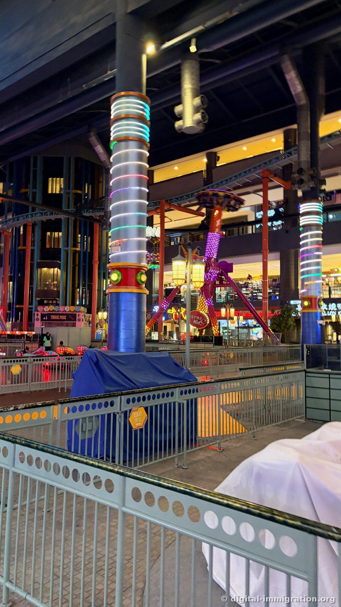 Indoor theme park ride covered with blue cloth and stopped, purple Spin Crazy behind with neon pillars