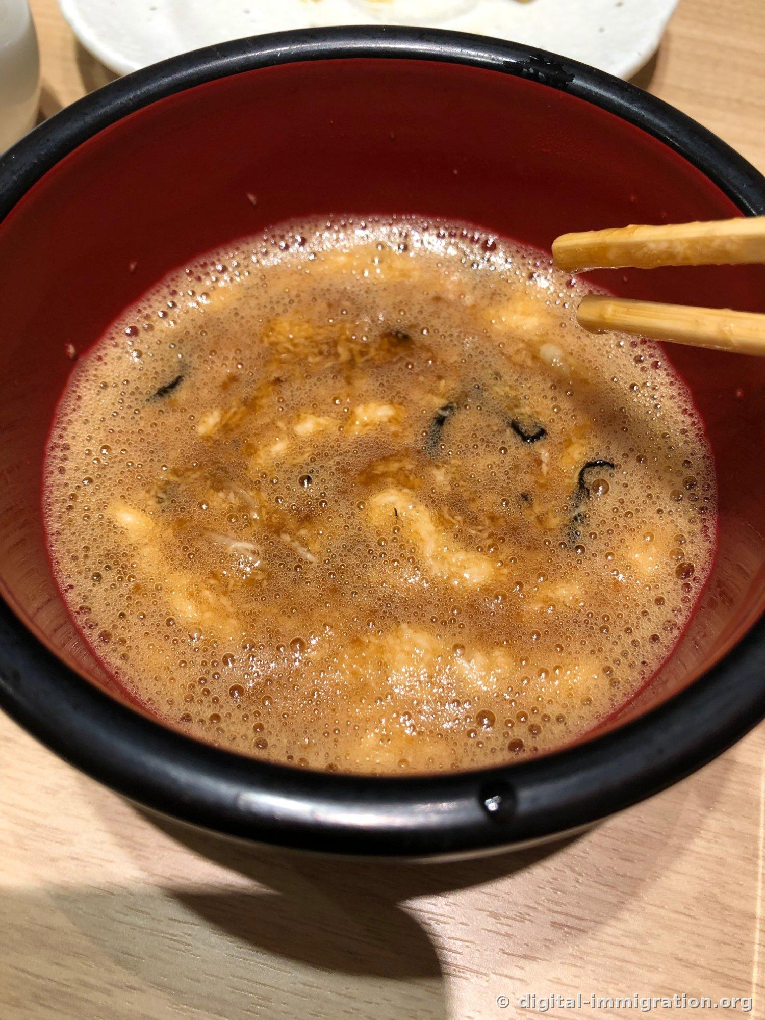 A bowl of foamy brown soup with nori floating in it after sobayu is poured in, with chopsticks resting on the rim