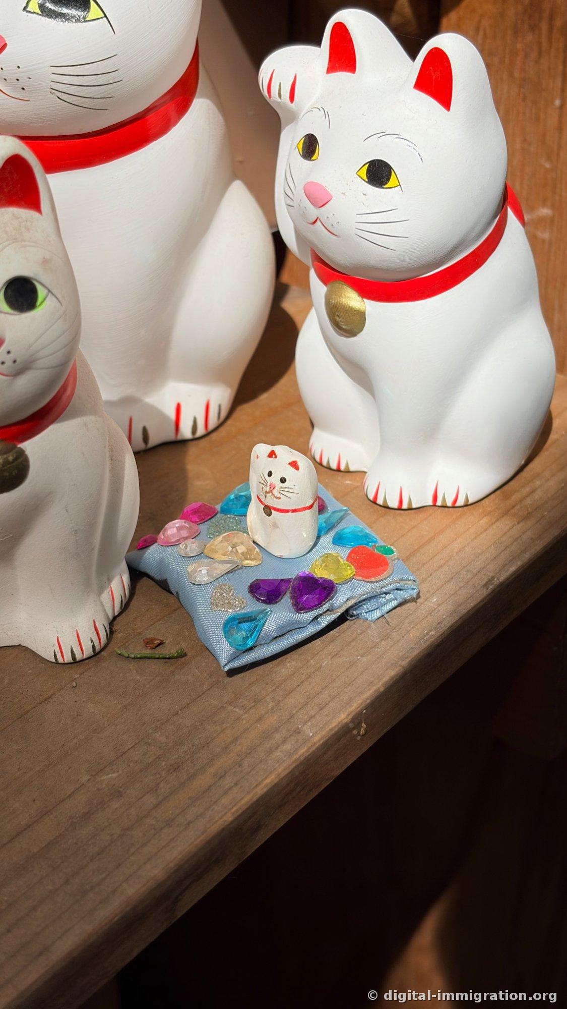A close-up photo of a finger-sized white cat sitting on a small cushion made from blue fabric with plastic jewels attached