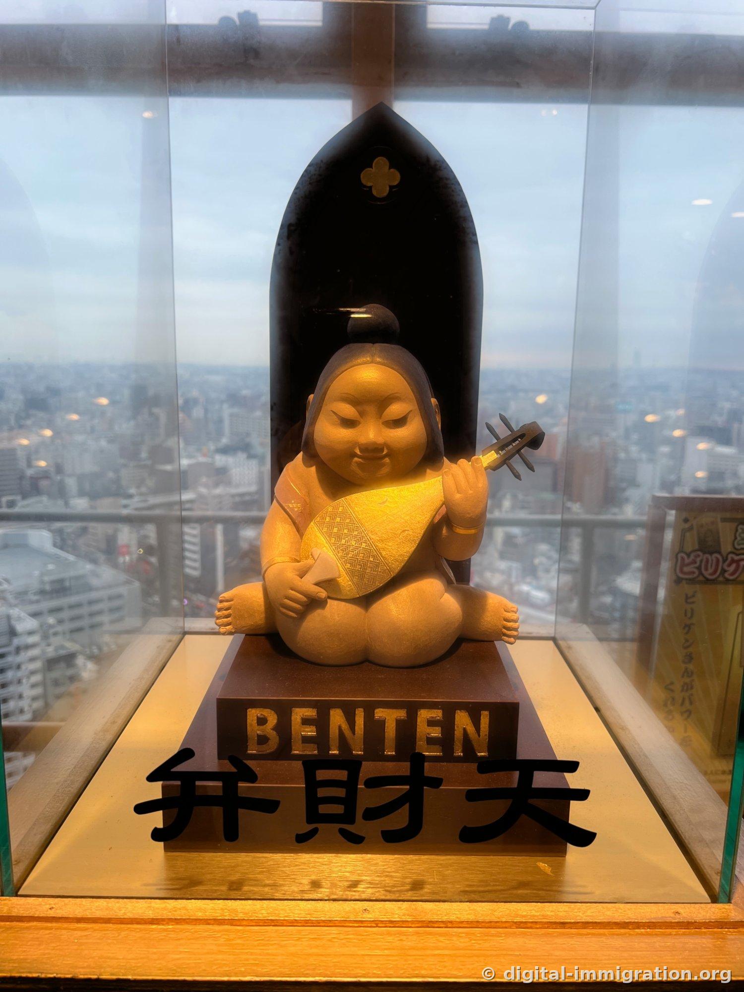 A wooden statue of Benten sitting and holding a biwa