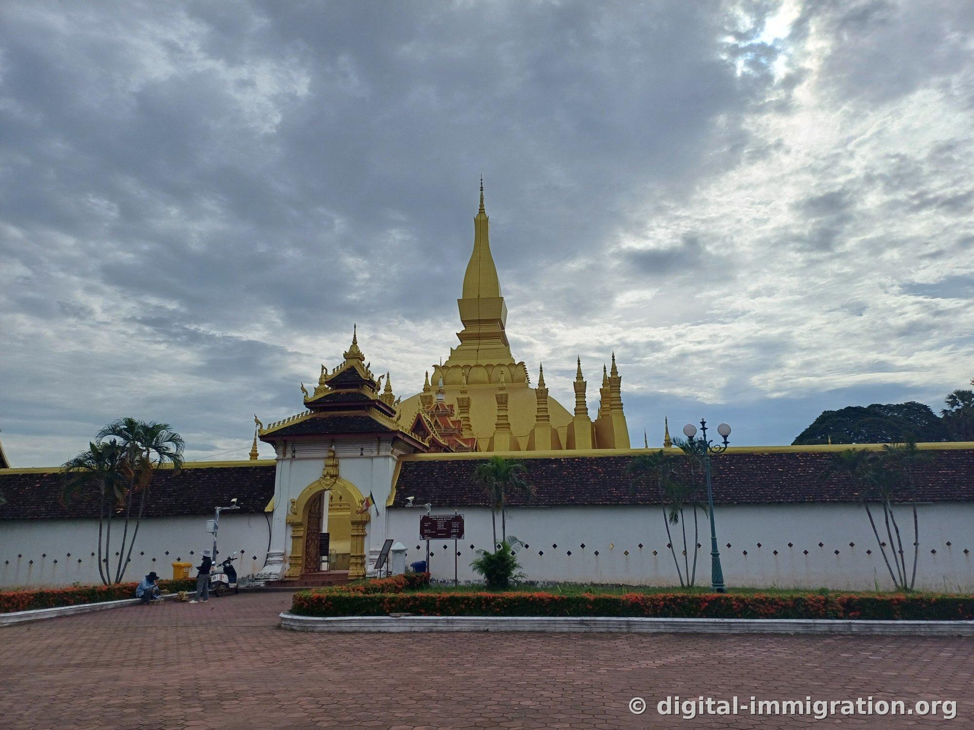 The entrance gate pavilion with information board and the golden stupa rising beyond the white wall