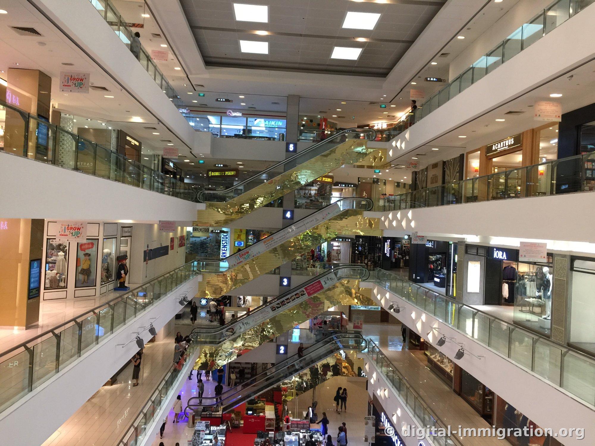 Vue intérieure du Centrepoint. Les enseignes BIRKENSTOCK, ROBERT PIANO, iORA, ACANTHUS sont visibles ainsi que plusieurs étages de balustrades en verre