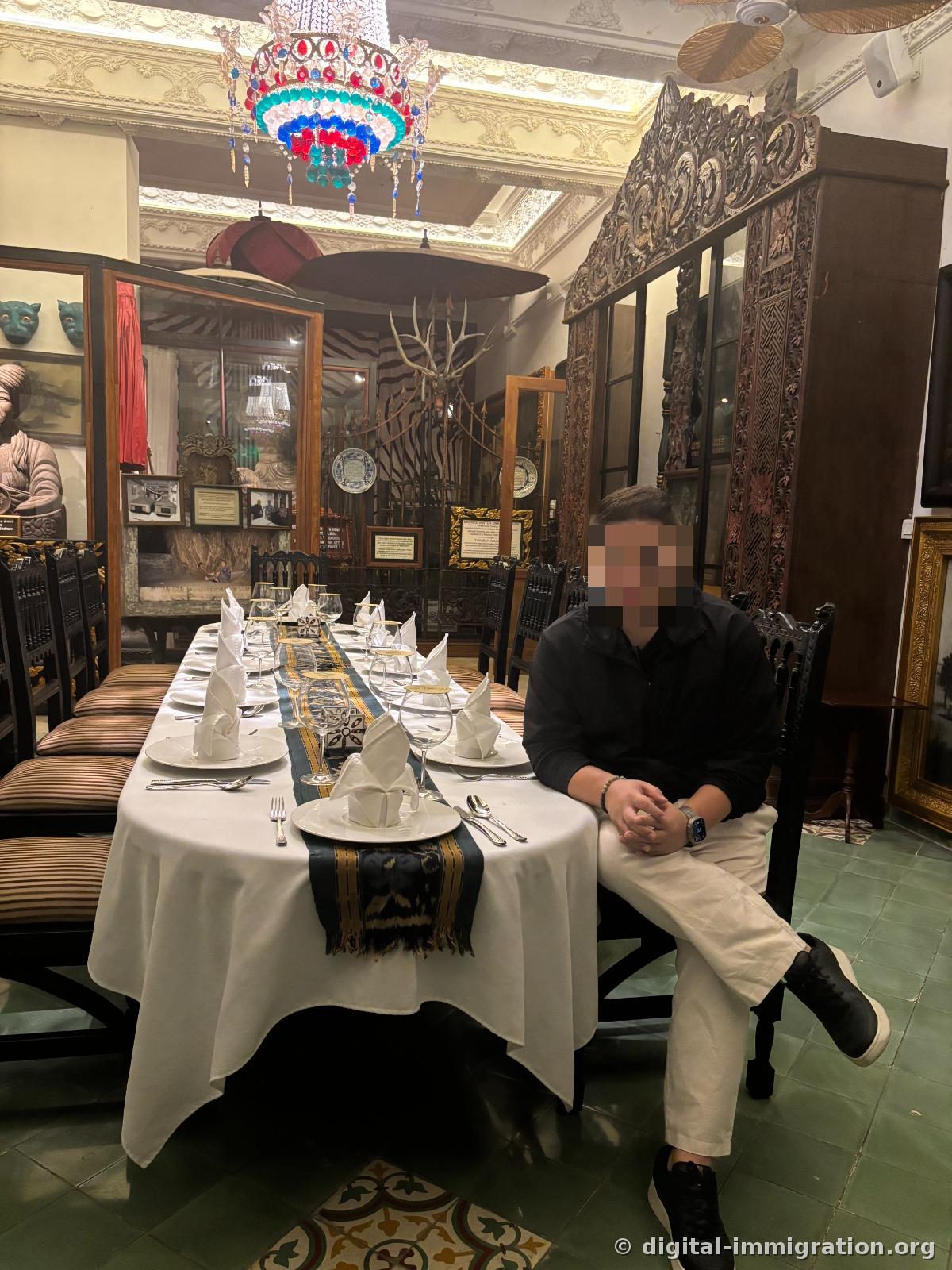 Dining room interior with glass bead chandelier above a long white table setting, artifact display cases and wooden partition screens behind