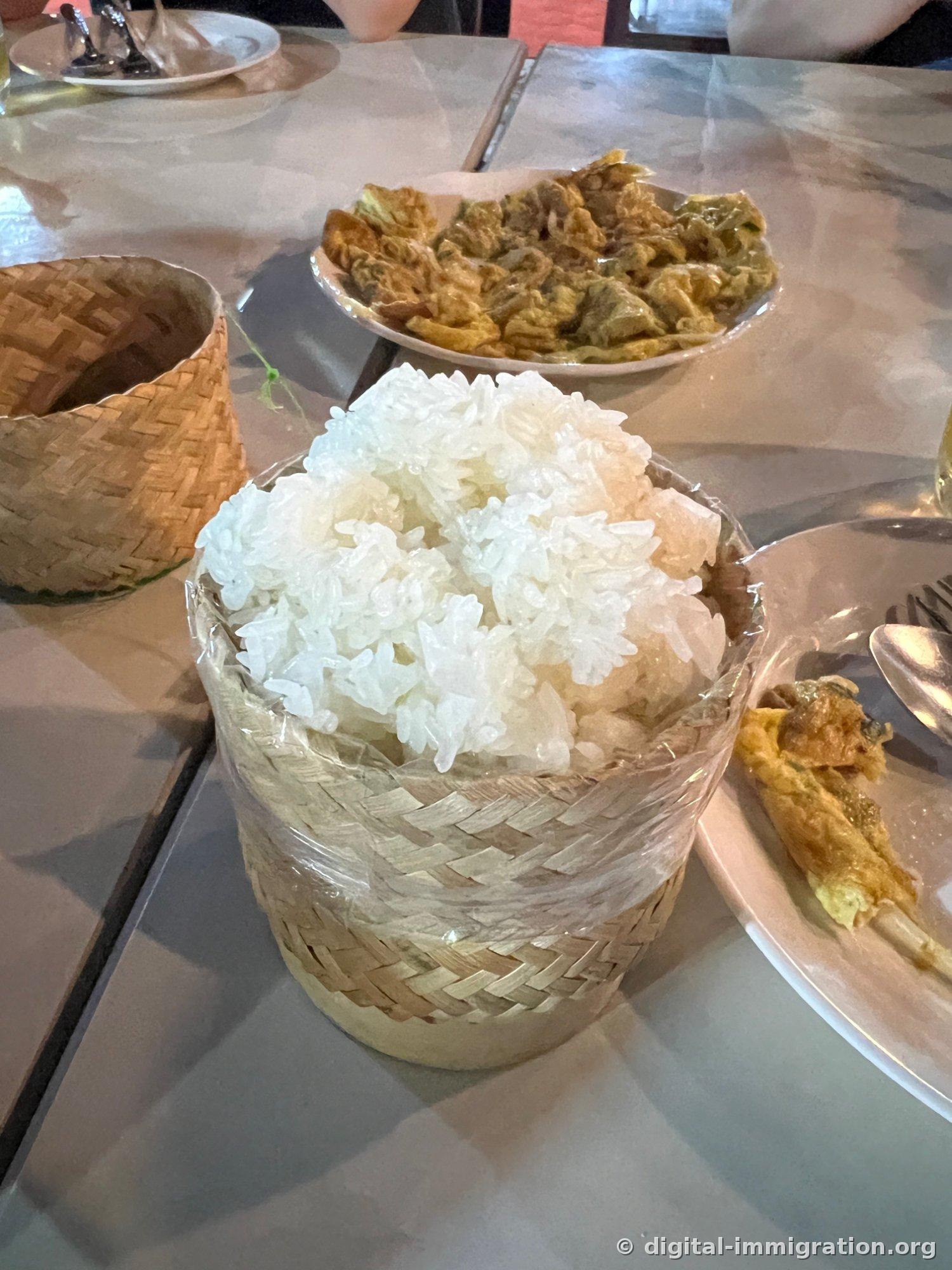用塑料膜裹着、装得满满的竹筒老挝糯米，后面放着蛋卷盘子，旁边有一个已经空了的竹筒盖子
