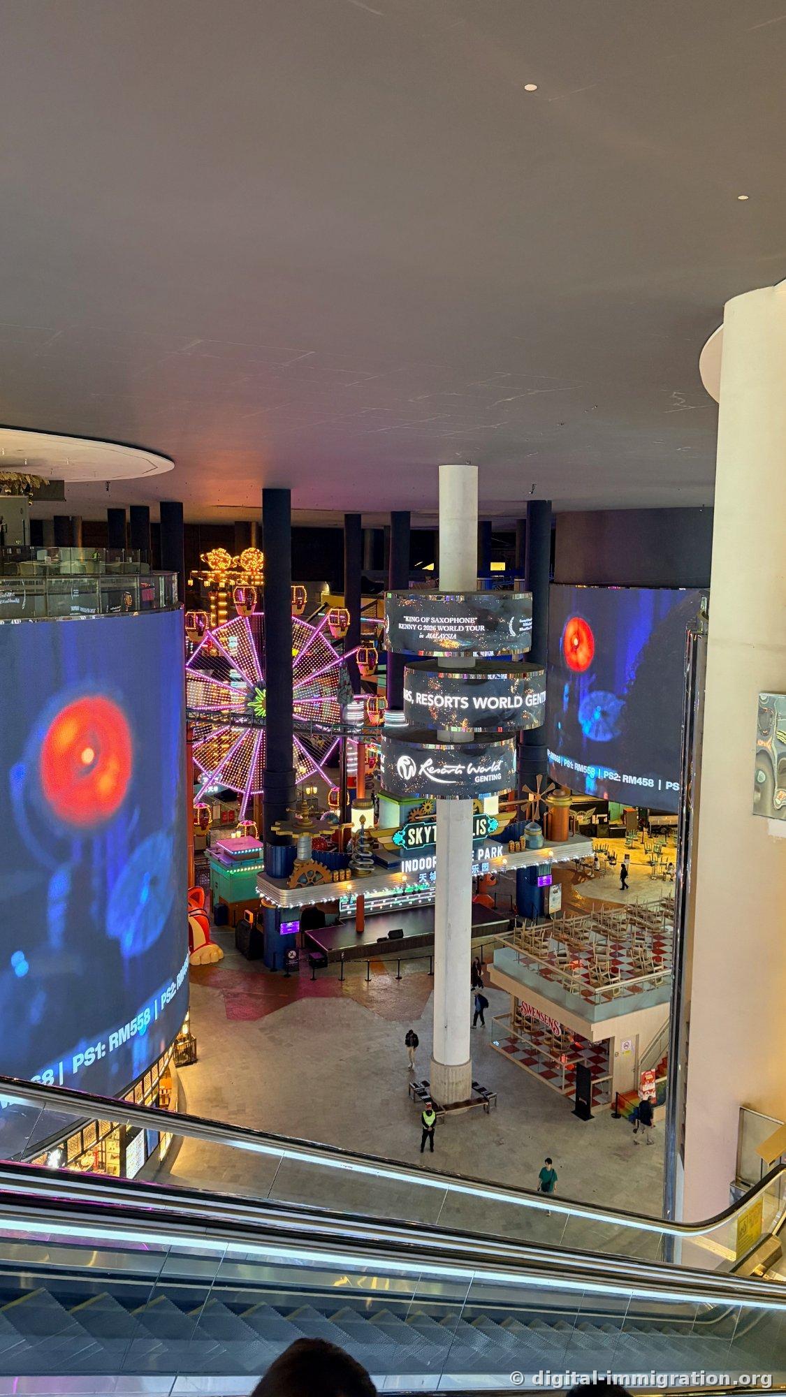 Looking down from escalator at indoor plaza with large LED screen and illuminated indoor Ferris wheel, SKYTROPOLIS INDOOR THEME PARK sign