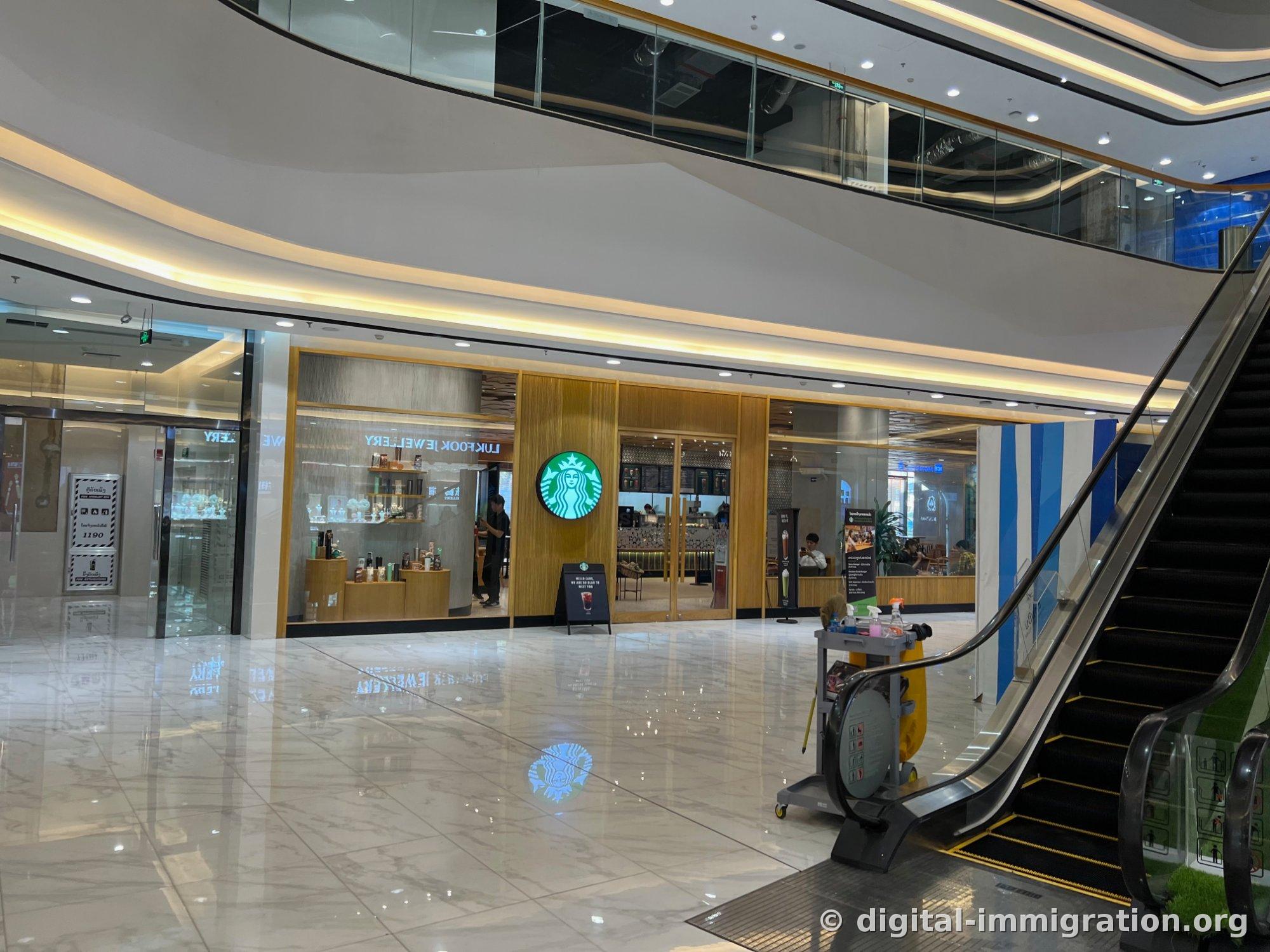 Façade du magasin Starbucks au Parkson Mall, avec le mur de couleur bois et le logo de la sirène verte, chevalet d'entrée A-frame, et escalator ainsi que chariot de nettoyage à droite