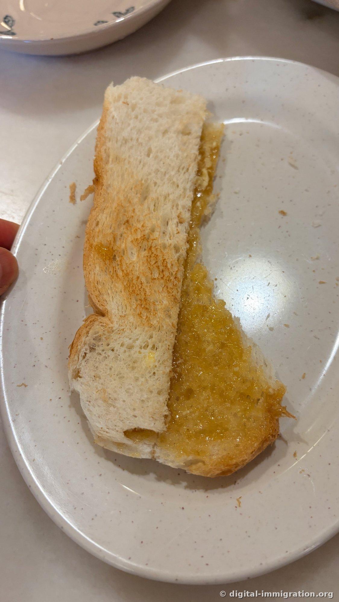 On a white plate sits toasted bread folded in half, with yellow kaya jam and butter generously spread on the cut side of the Roti Bakar