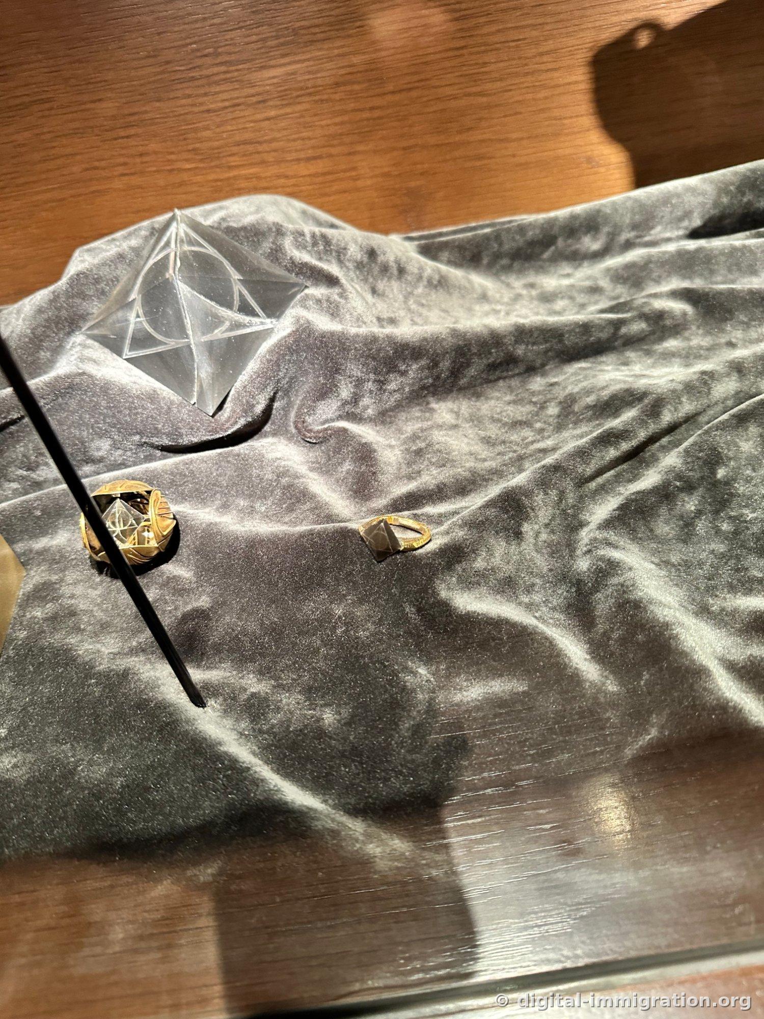 Two gold rings and a transparent crystal sculpture with the Deathly Hallows symbol photographed at an angle
