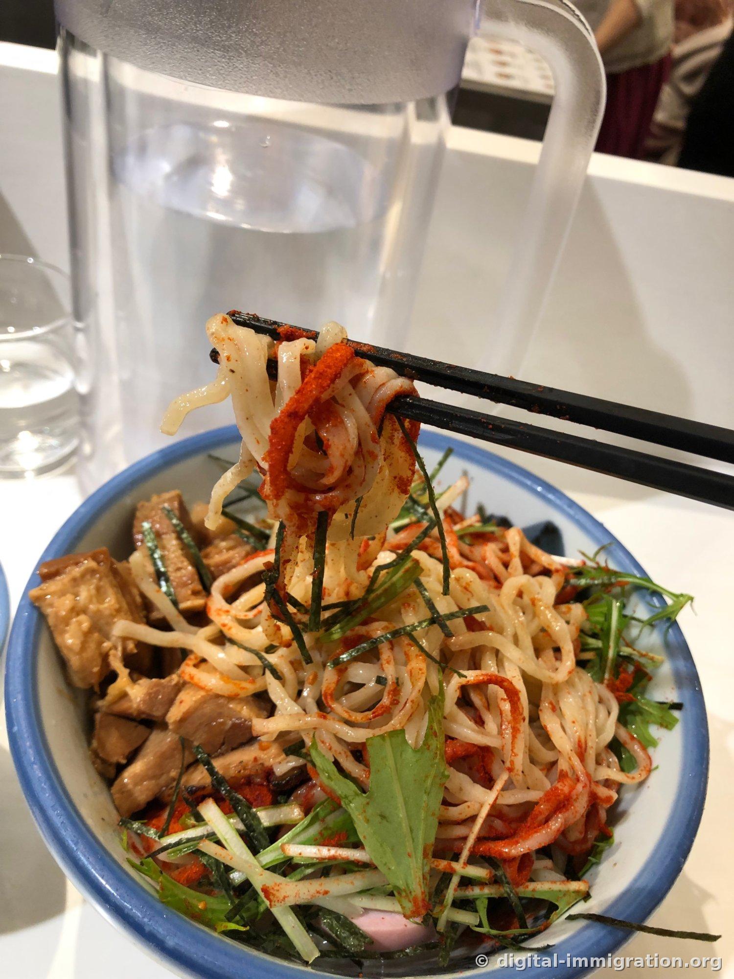 First chopstick lift of broth-free noodles with red chili powder, with shredded seaweed, mizuna, bamboo shoots, and meat pieces in the bowl