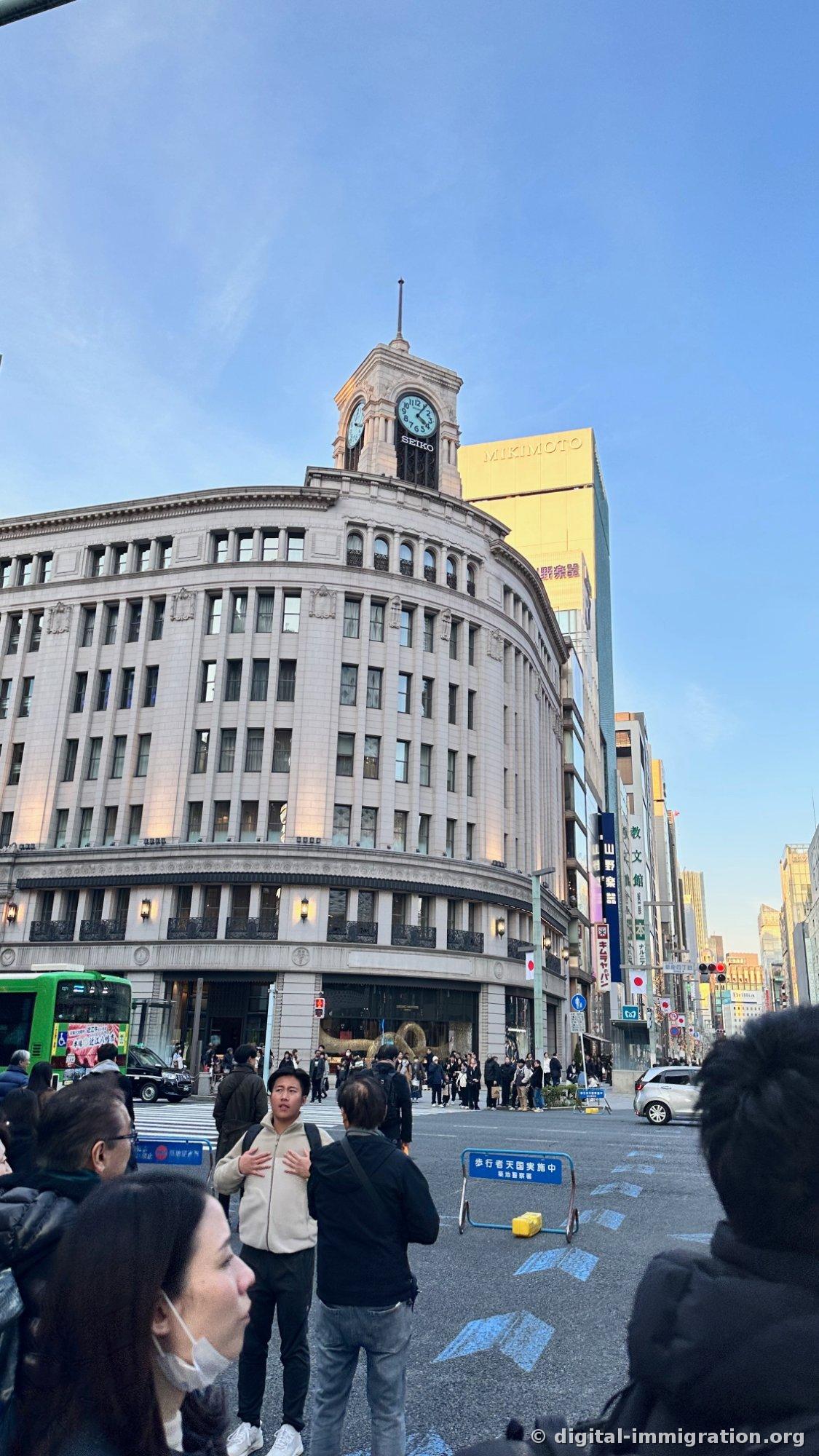 Winter evening scene of people standing on Ginza intersection road with pedestrian paradise sign, looking at Wako clock tower