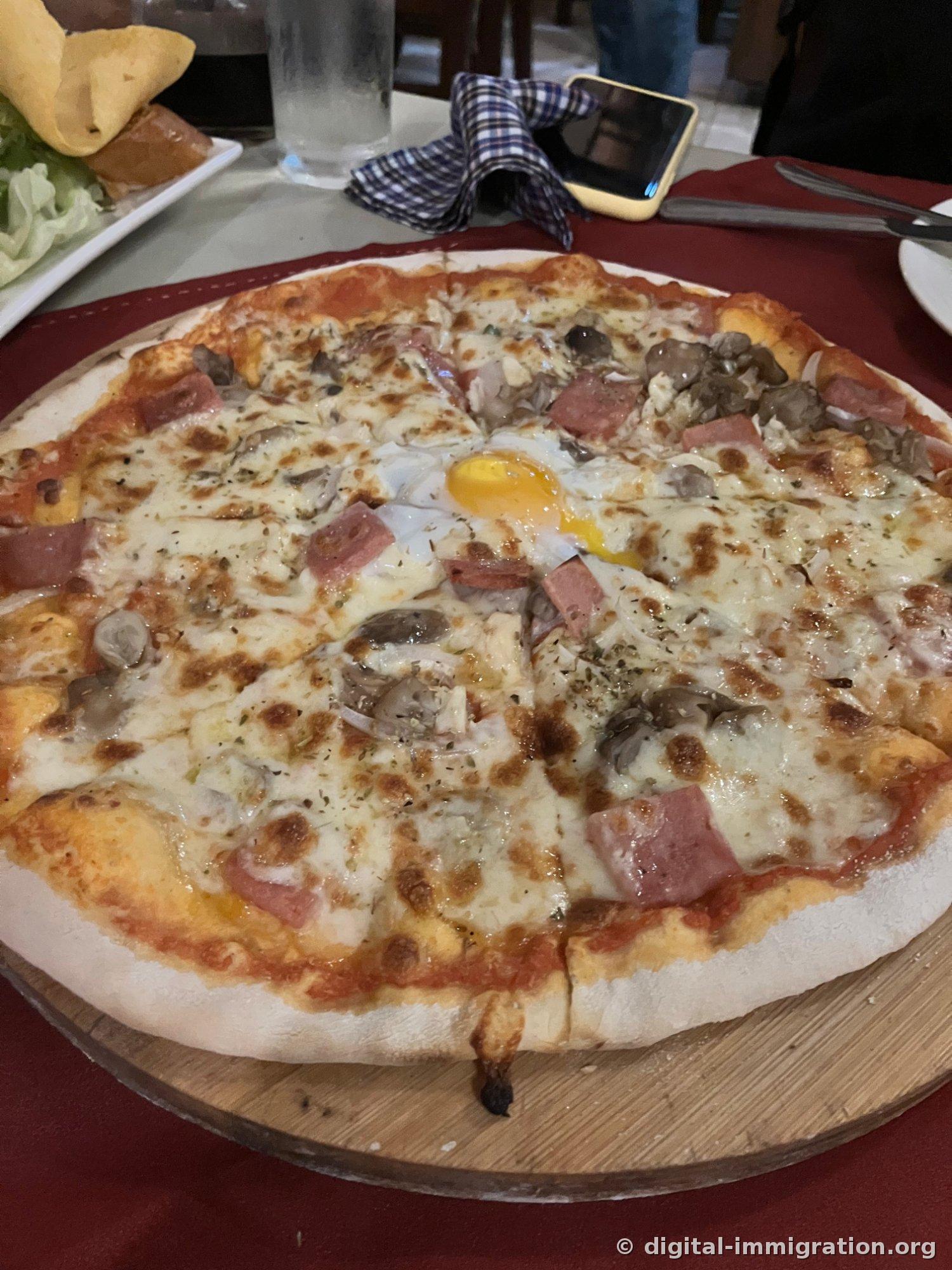 Wood-fired pizza on a wooden board with ham and mushrooms covering the cheese, a soft-cooked egg yolk in the center