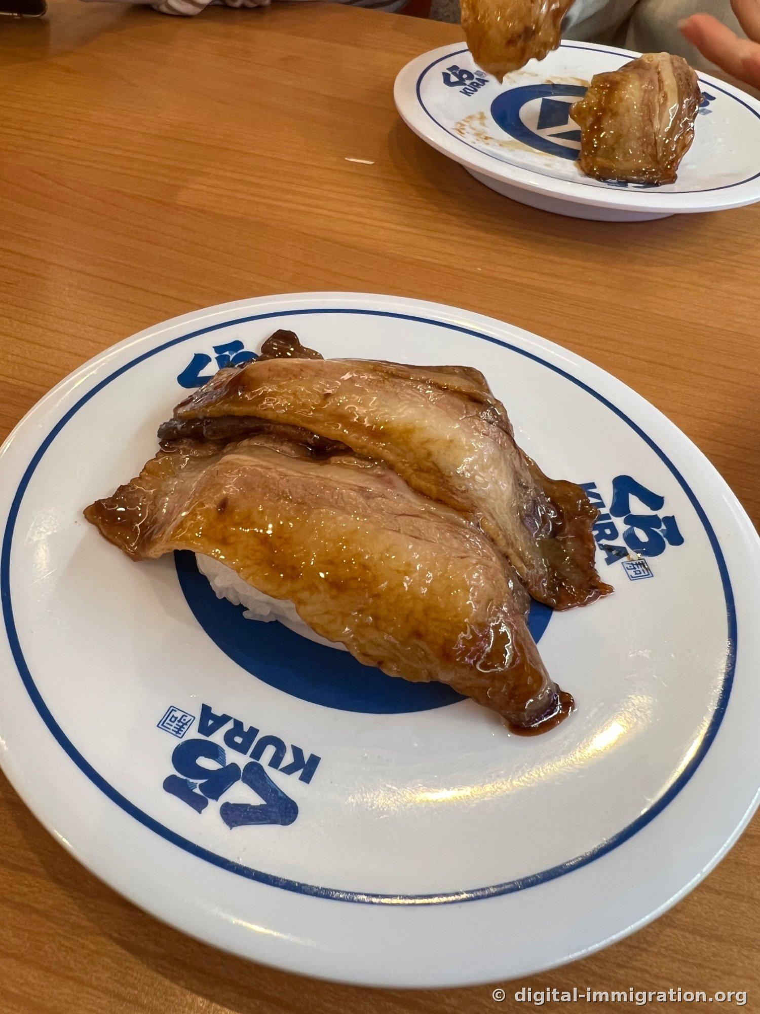 간장 소스가 발린 큼직한 차슈 두 장이 밥을 덮고 있는 초밥, 뒤쪽 접시에는 반쯤 먹은 차슈가 놓여 있다