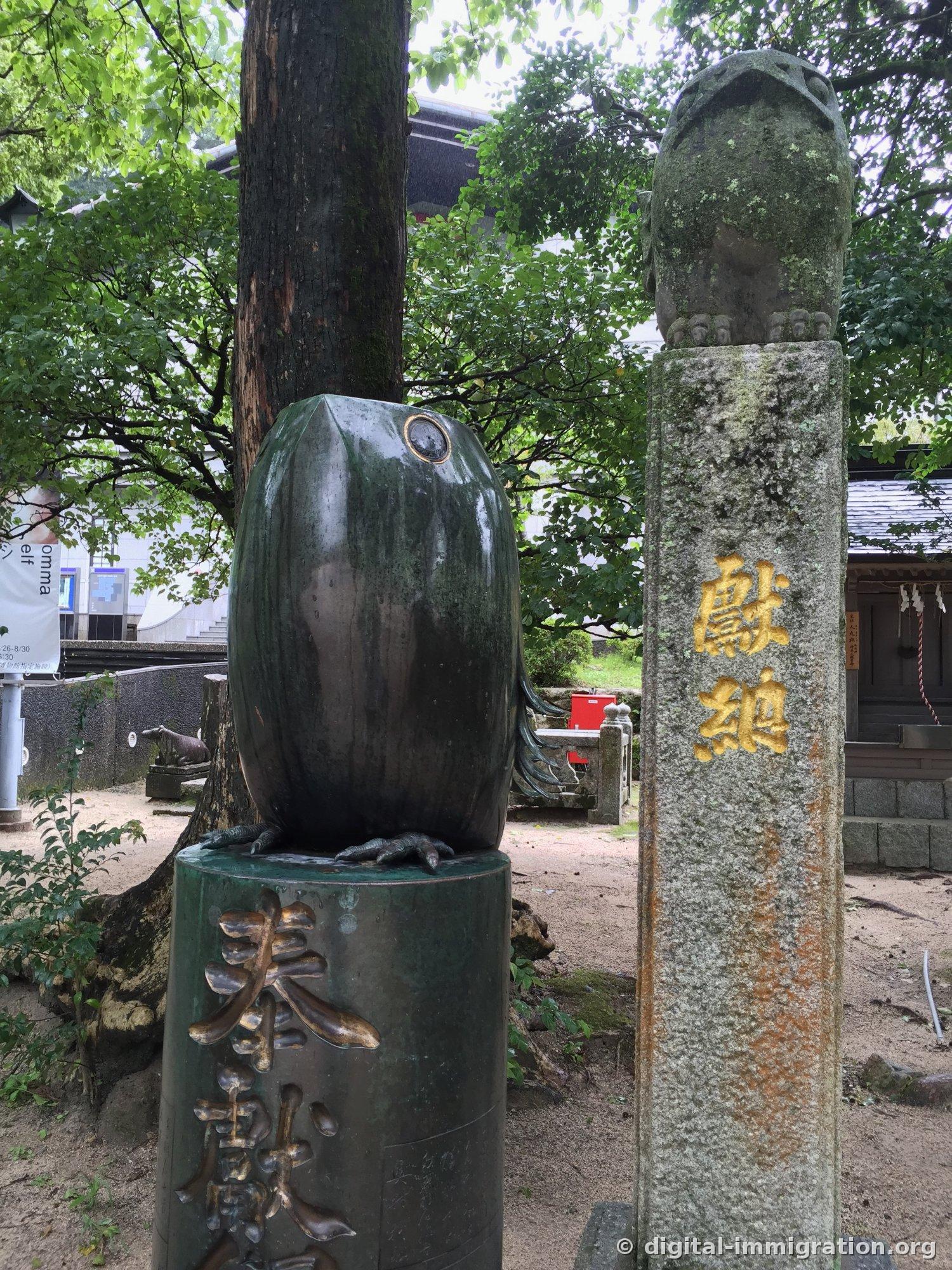 Round-bodied bronze uso bird statue with a stone pillar inscribed in gold '獻納' beside it