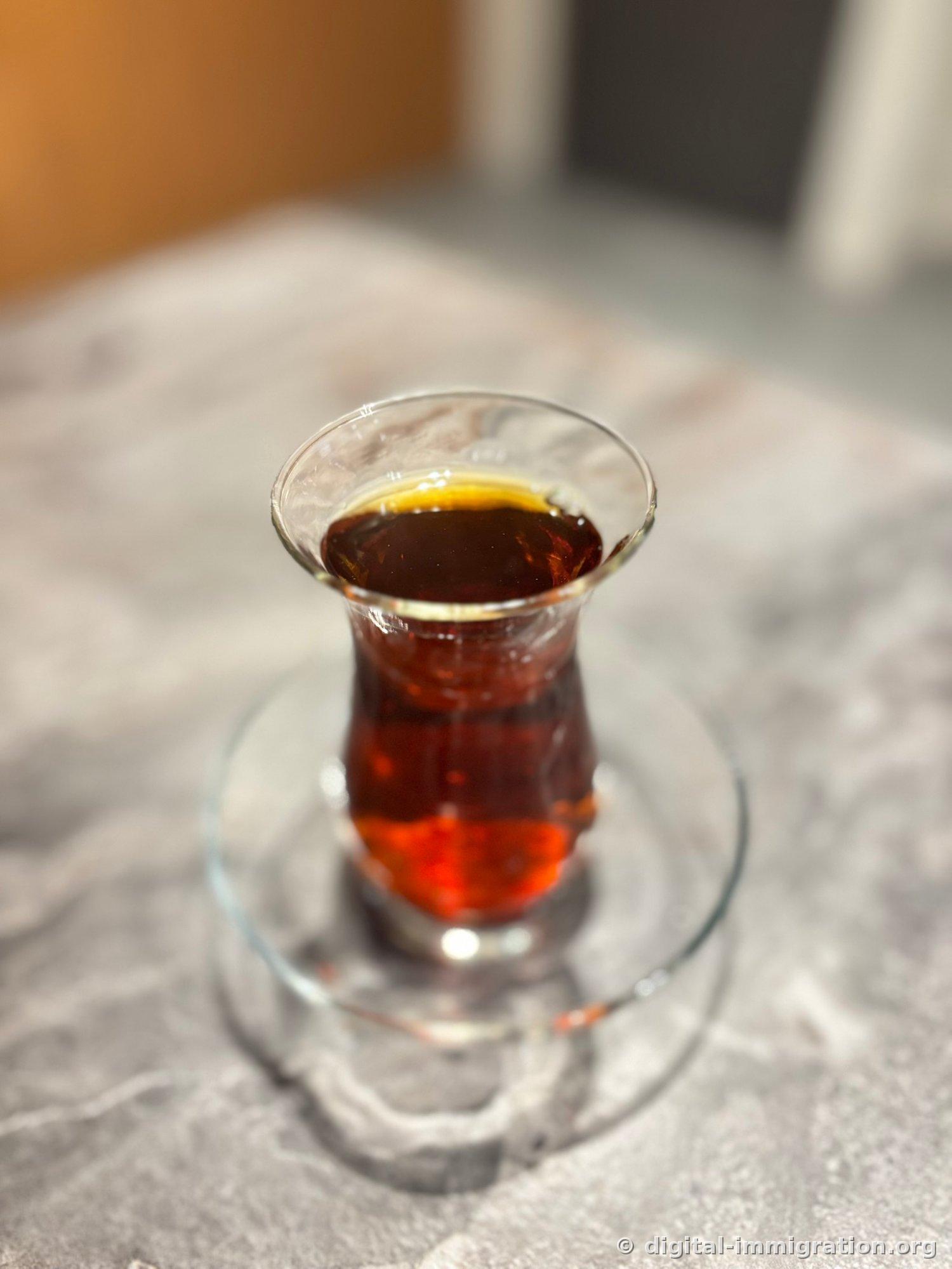 Turkish black tea 'çay' with a deep reddish color in a tulip-shaped glass on a glass holder placed on a marble table
