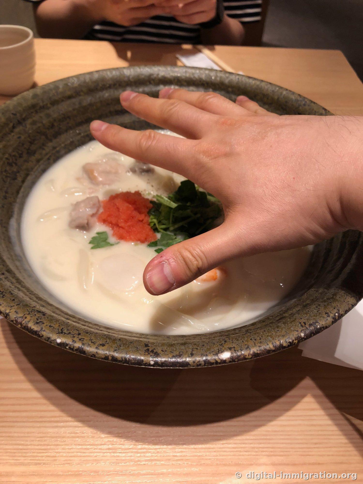 Hand spread over the cream udon bowl to compare sizes, the hand cannot fully cover the inside of the bowl