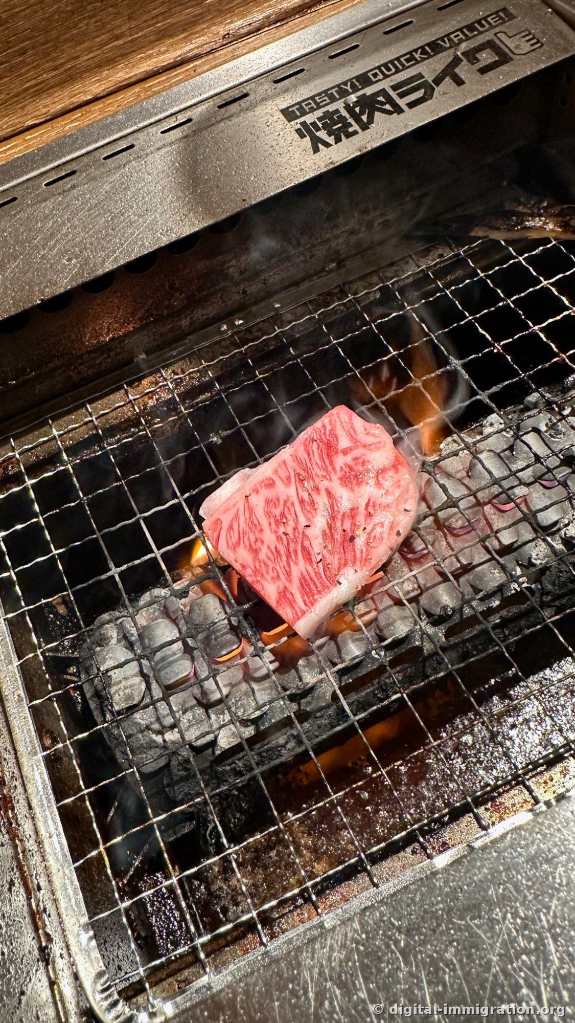 Un morceau de wagyu finement marbré posé sur la grille du foyer à charbon, avec des flammes rouges qui montent depuis le bas