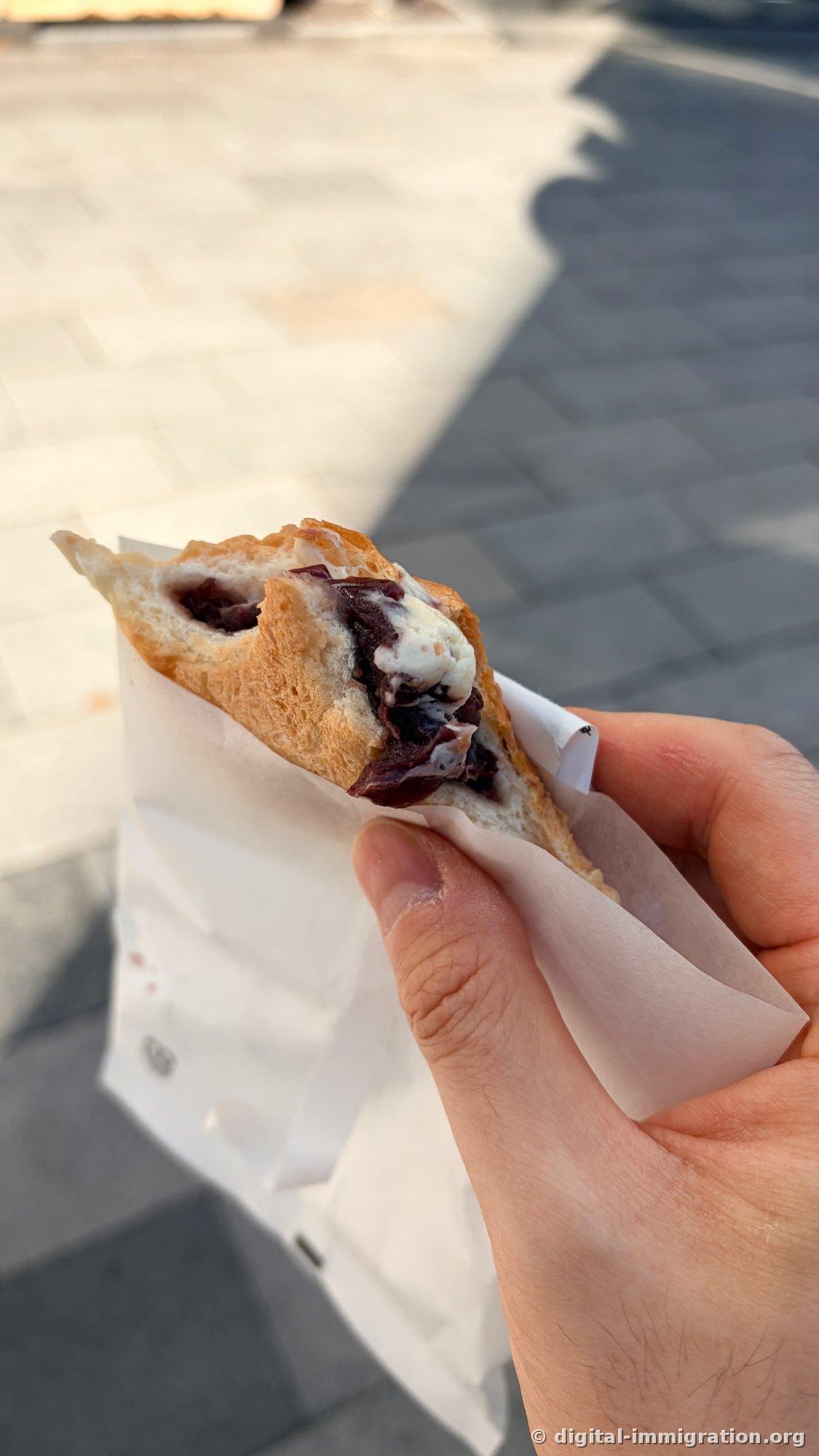 Cross-section of bitten anpan showing whole red beans and white cream leaking from dough