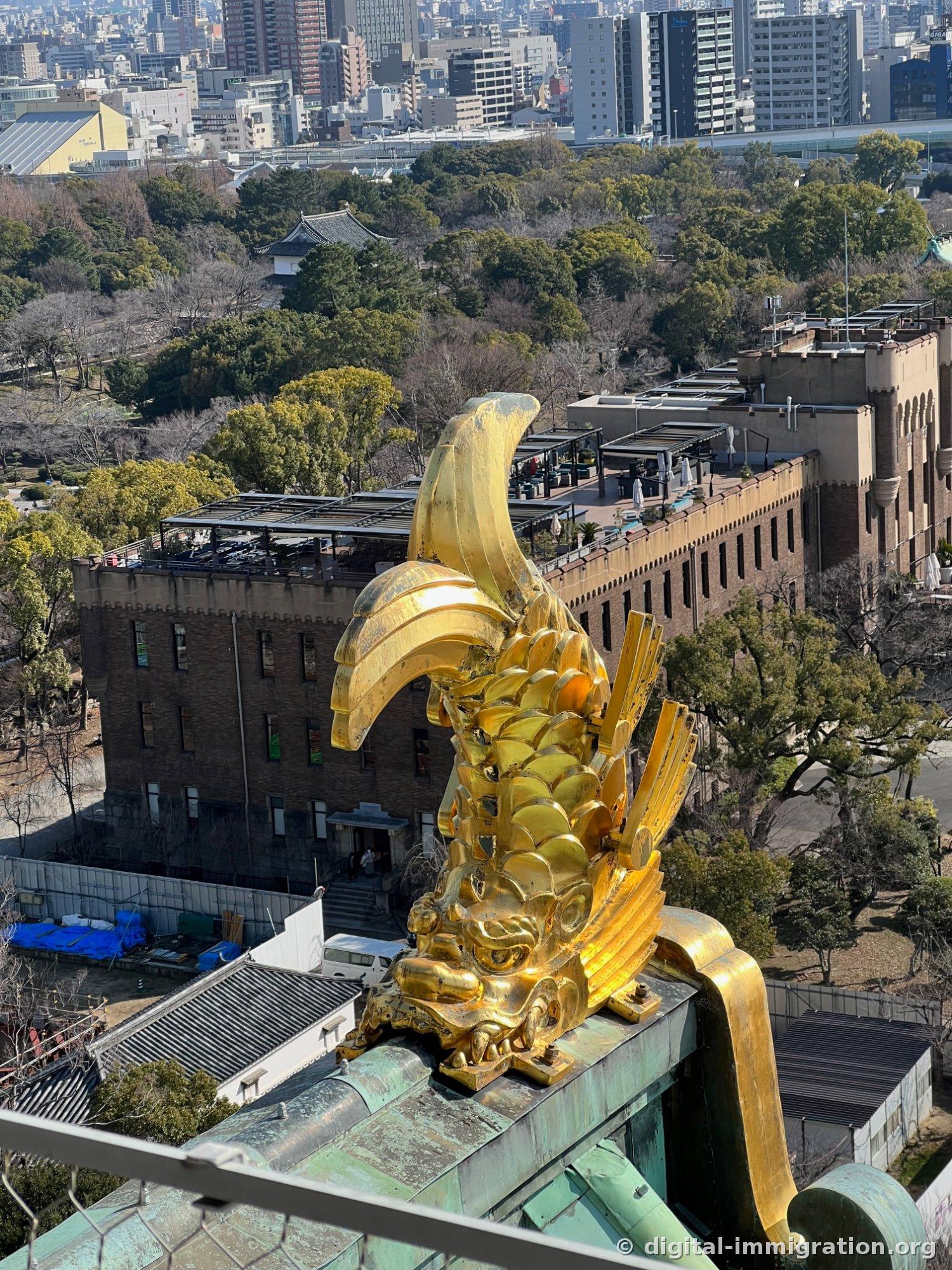 Vue depuis la plate-forme d'observation de la tour de guet du Shachihoko doré sur le toit et le bâtiment de brique en dessous, la forêt du parc, et la ligne d'horizon d'Osaka au loin