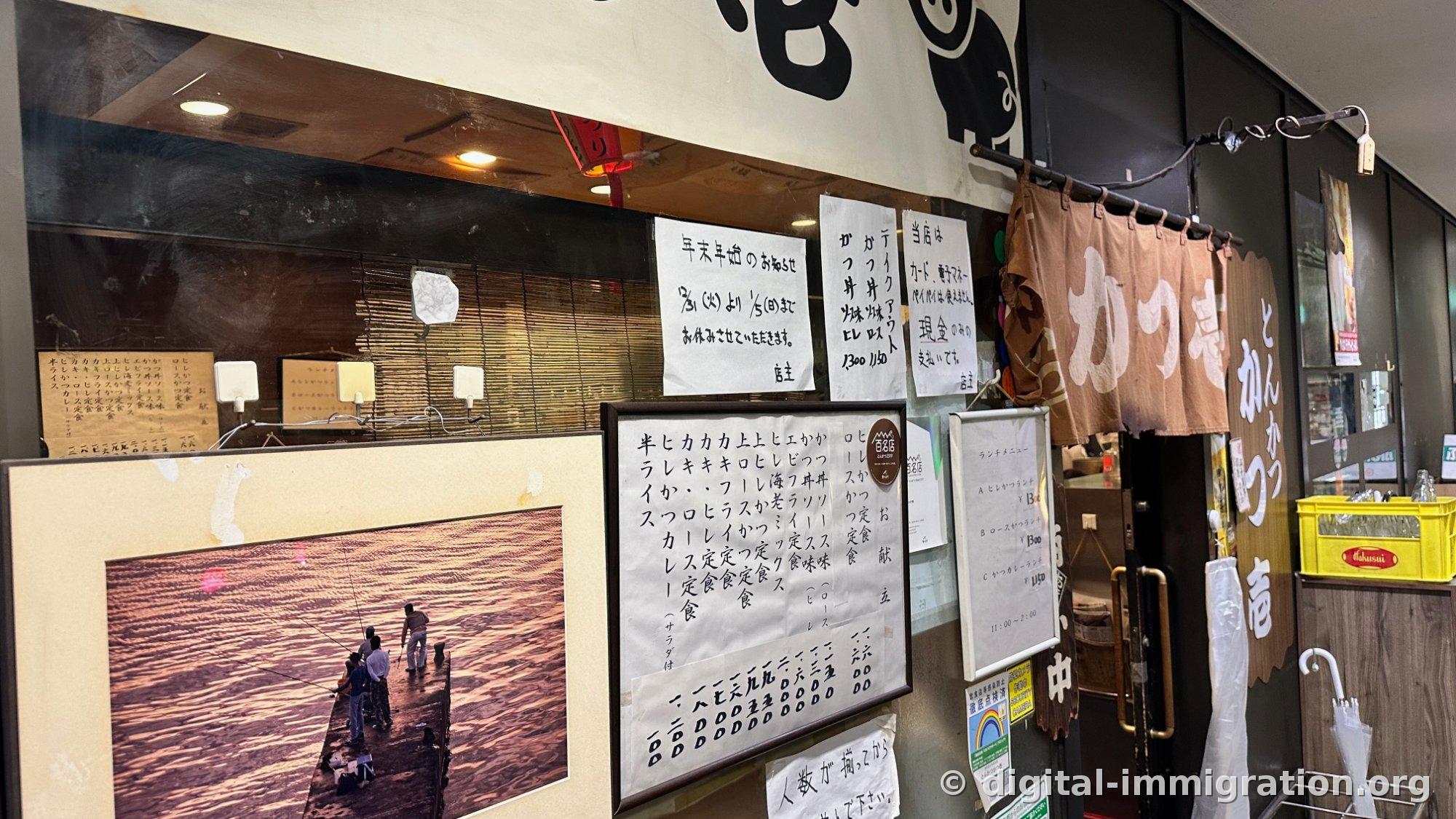 The shop entrance with handwritten menu frames, cash-only notices, and brown noren curtain