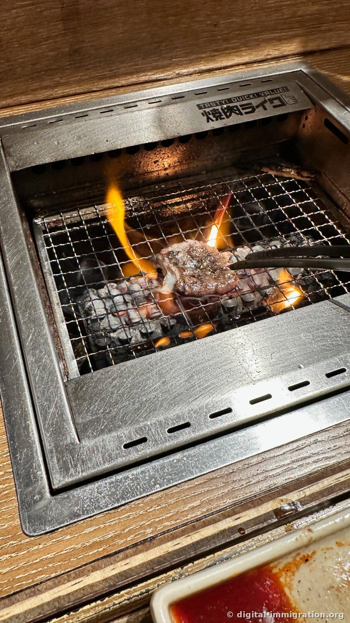 De la graisse tombe sur les charbons créant une grande flamme orange, avec un morceau de viande qui cuit au cœur de la flamme